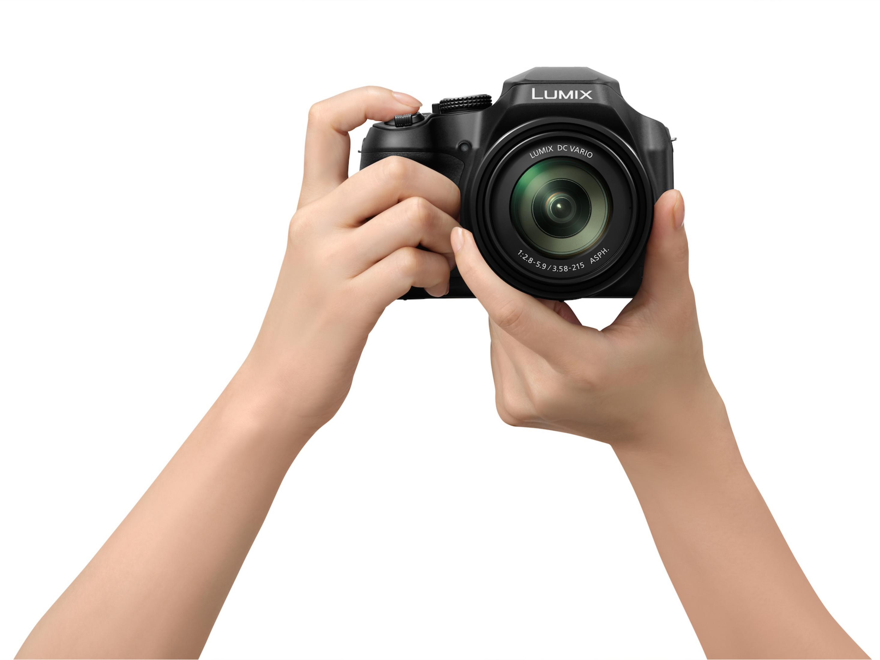 Hände halten eine schwarze Lumix Kamera. Das Objektiv befindet sich in der Mitte.