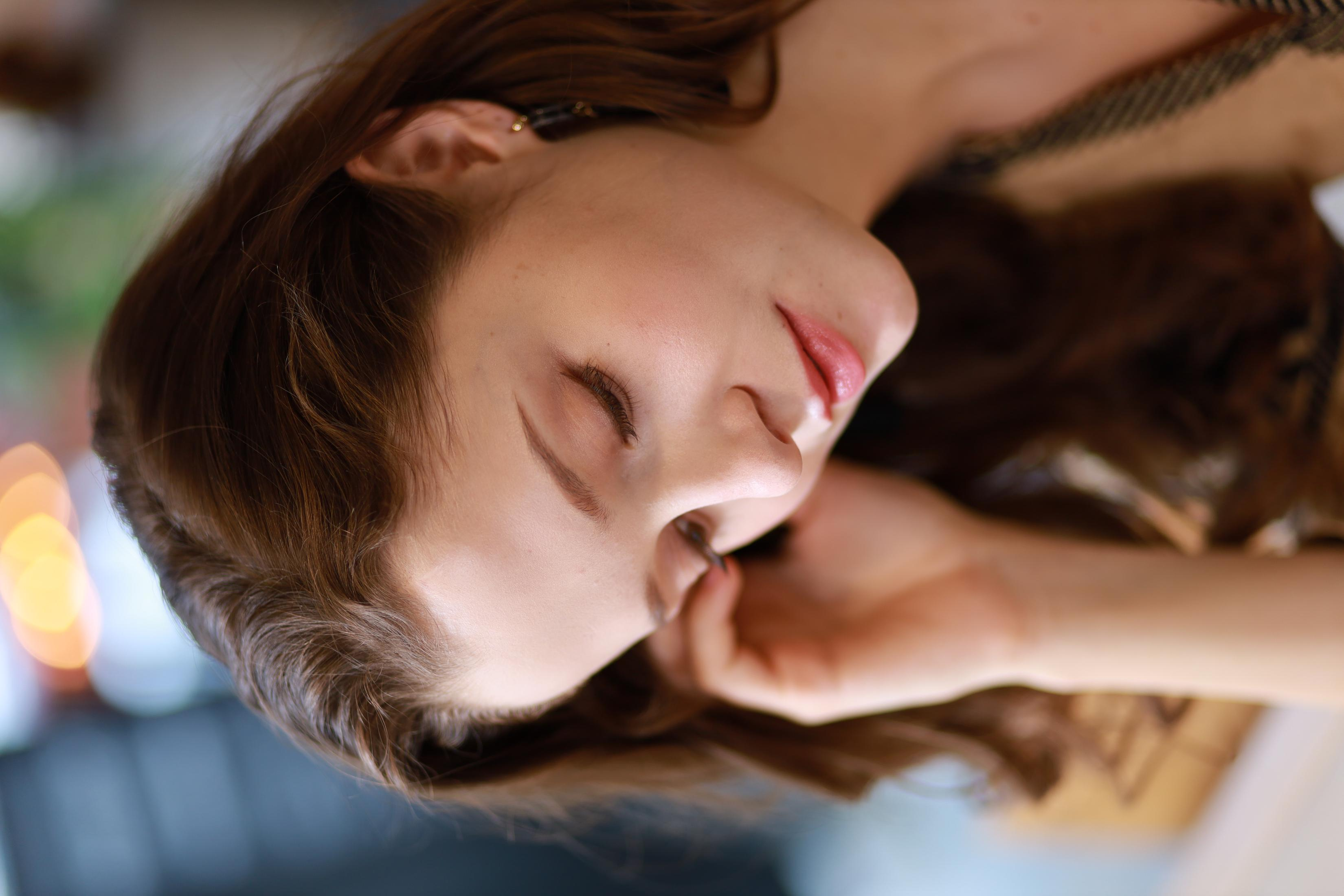 Una mujer con cabello castaño se muestra, mirando hacia abajo con los ojos cerrados, en primer plano.