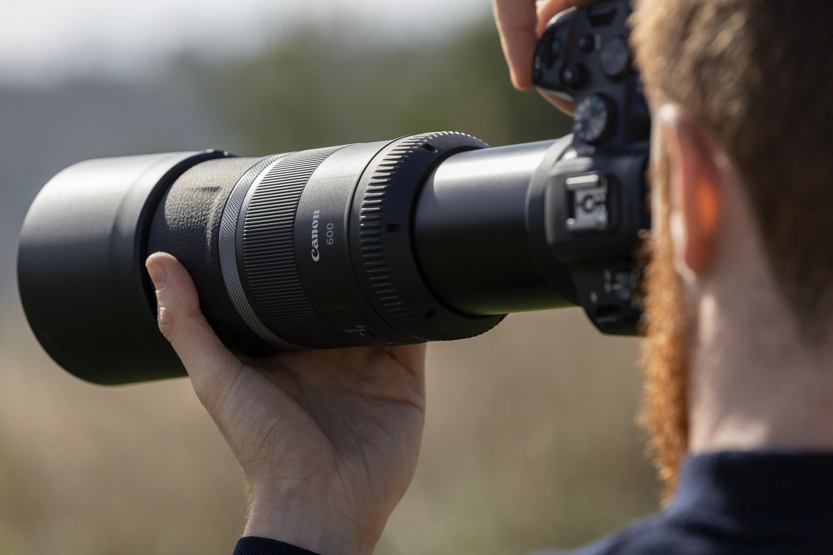 Eine Person hält eine große Canon-Linse mit angeschlossener Kamera im Freien bei Tageslicht.