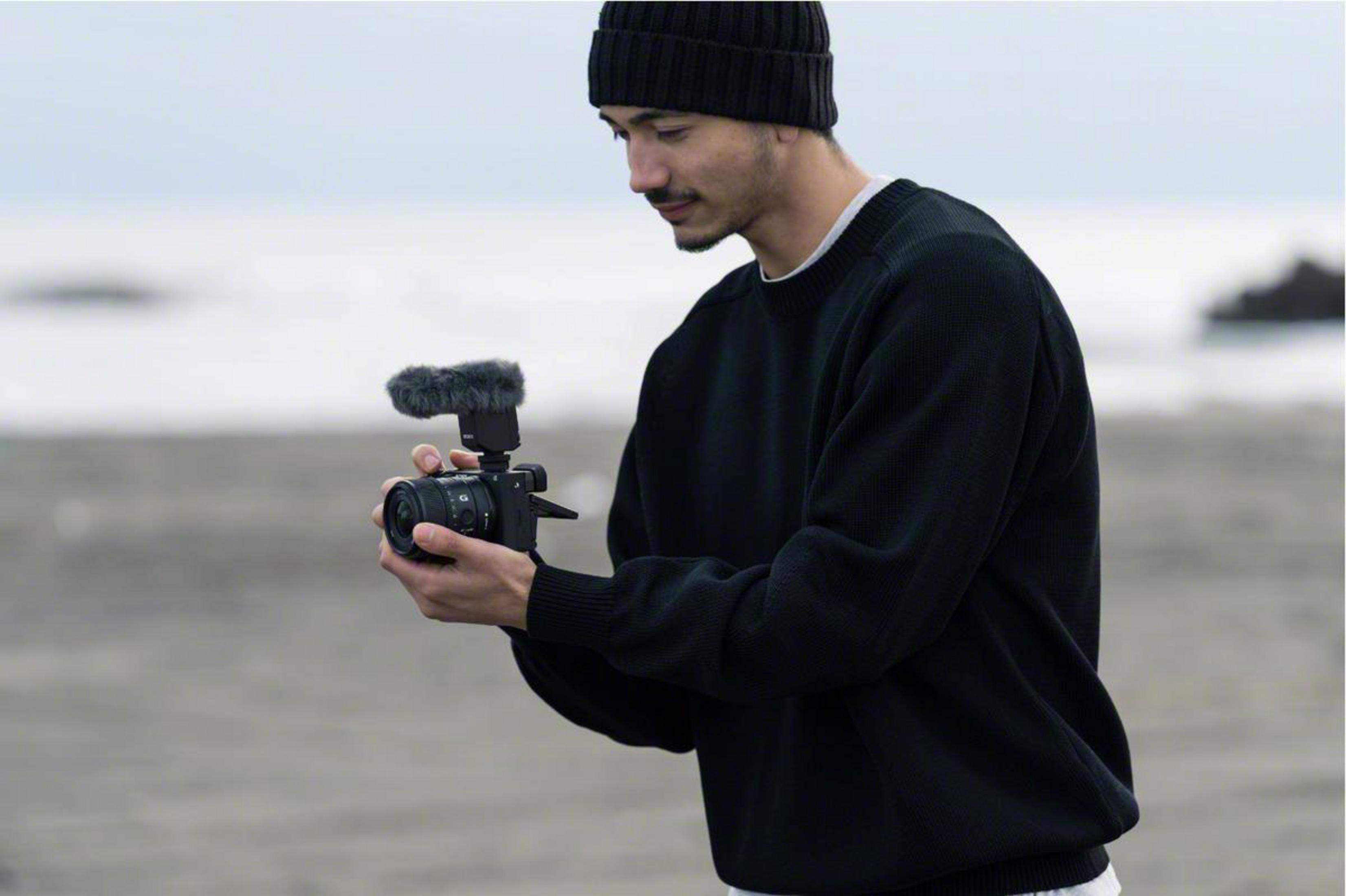 Mężczyzna filmuje kamerą, trzymając ją z mikrofonem, na plaży.