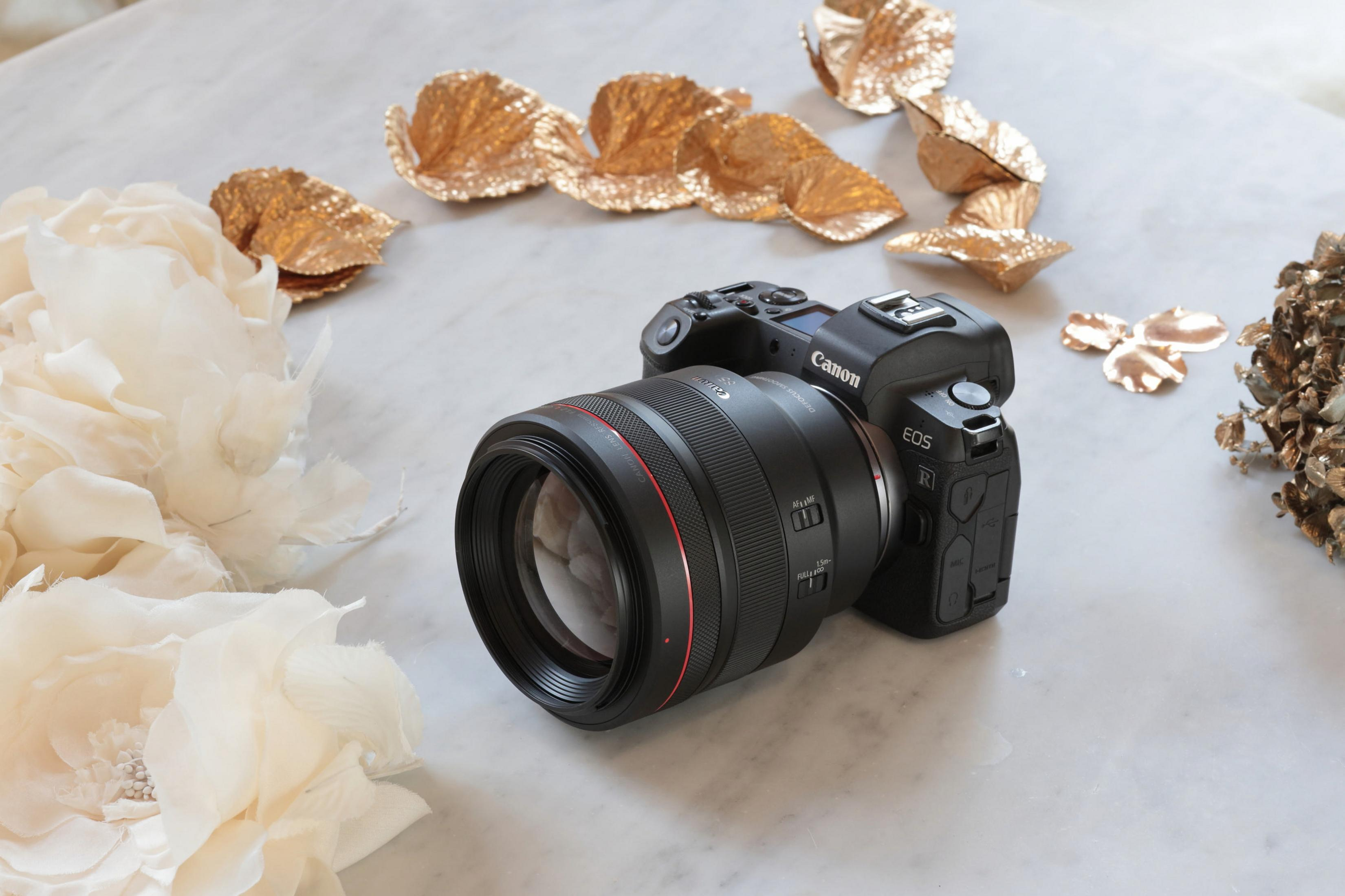 Eine Canon EOS R Kamera mit Objektiv auf einer Marmoroberfläche, umgeben von Blumen und Golddekor.