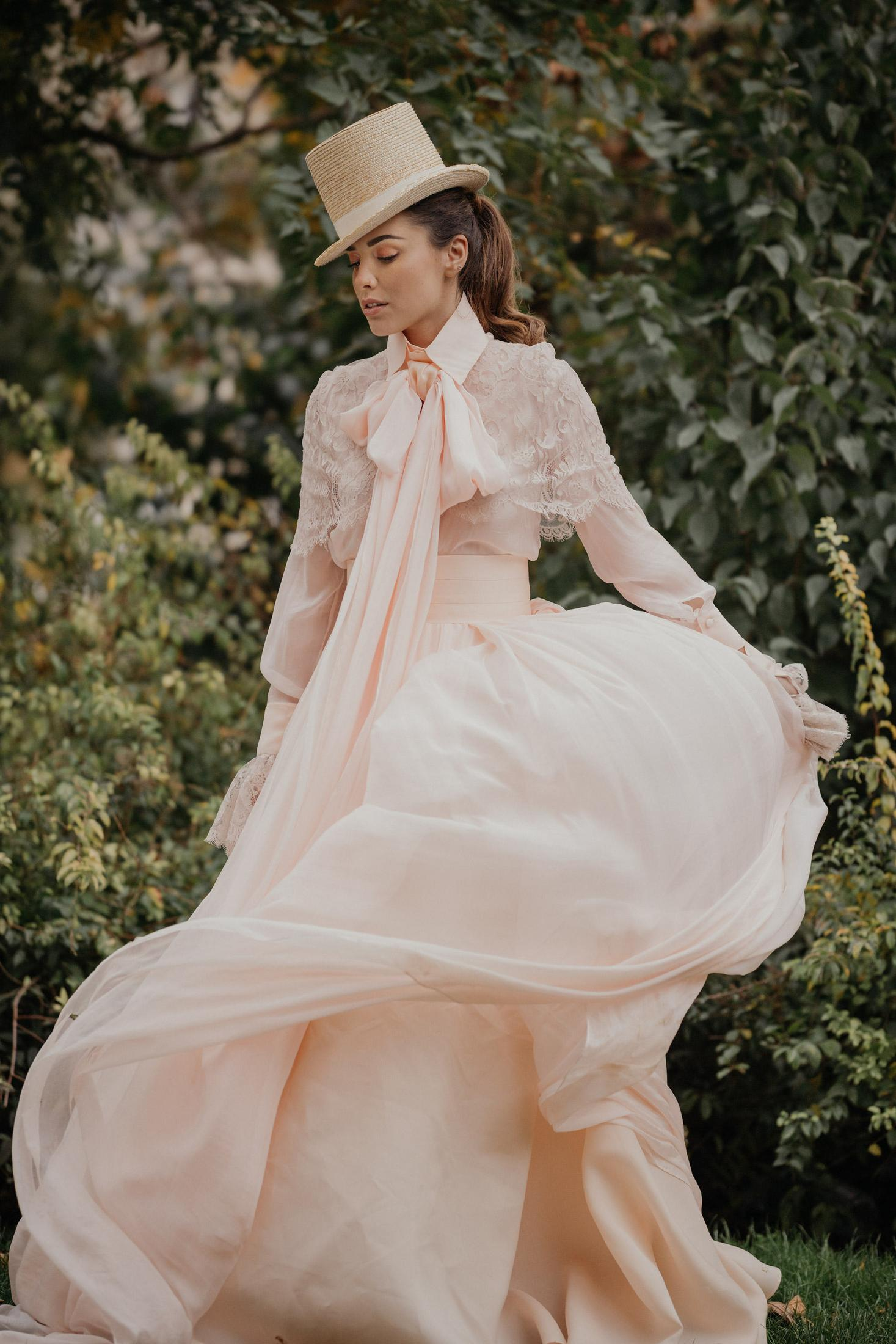 Frau in pinkfarbenem Kleid und Hut in einem Garten, mit fließendem Kleid.