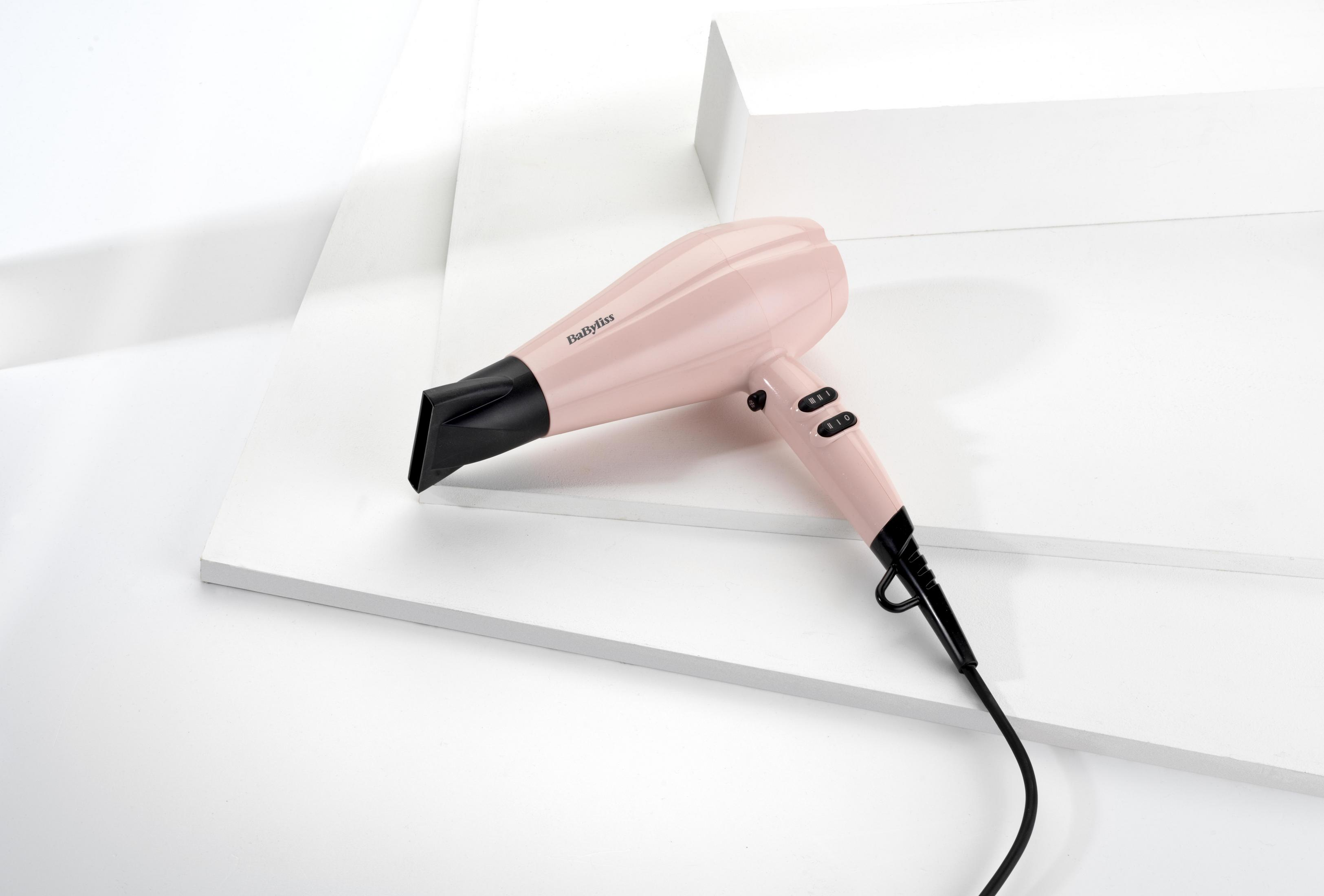 Różowa suszarka do włosów na białej powierzchni, czarna dysza, białe tło.
