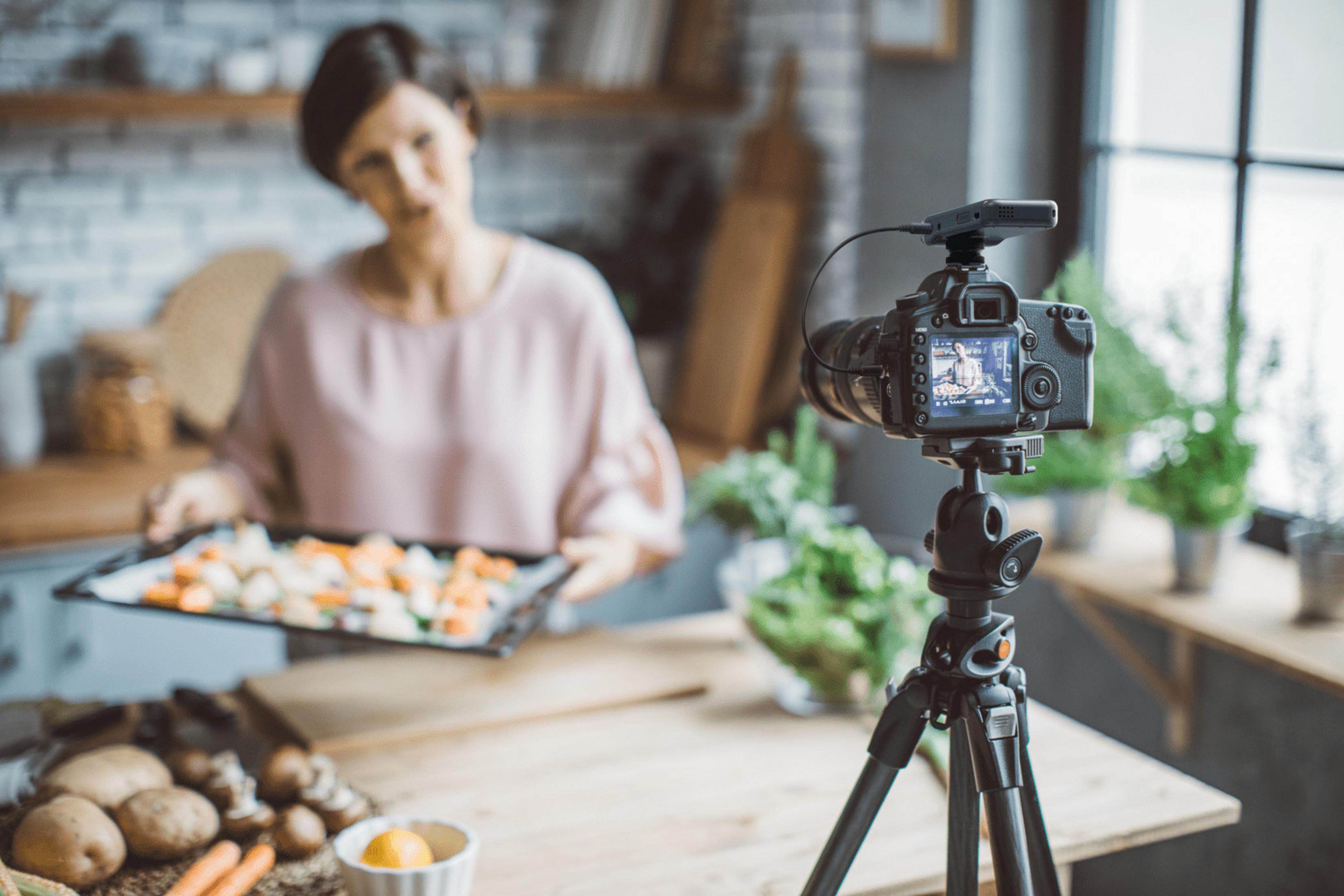 Kobieta kręci film o gotowaniu. Kamera na statywie, jedzenie na blasze.