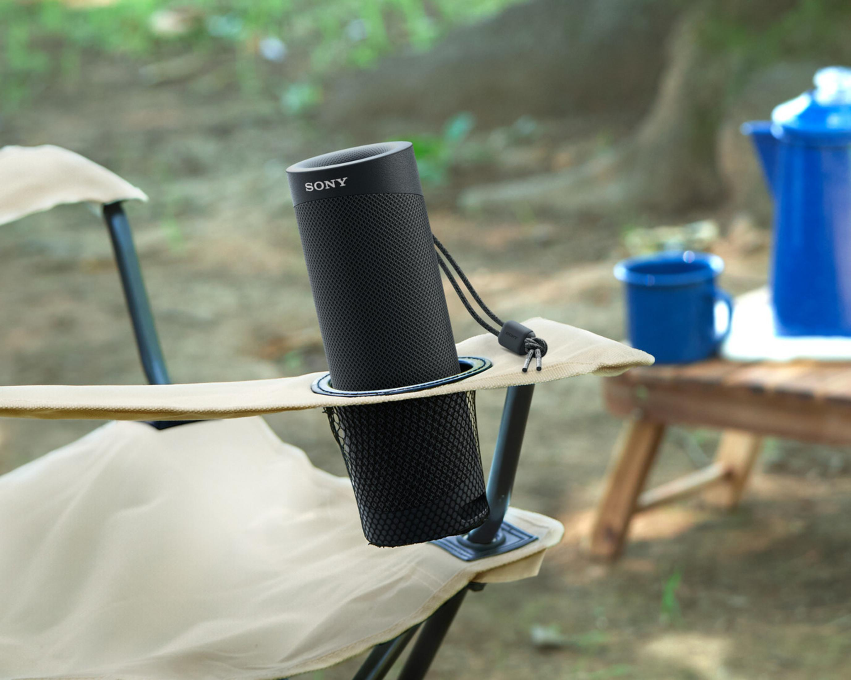 Altoparlante Sony nero in un portabicchieri su sedia. Alberi verdi sullo sfondo.
