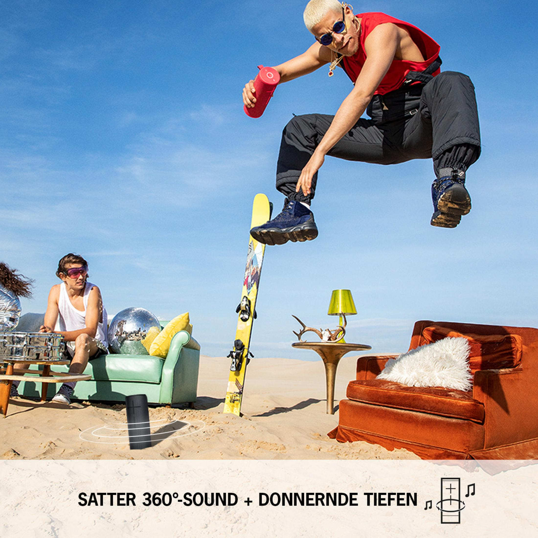 Mężczyzna skaczący ze snowboardem na plaży z innymi ludźmi i głośnikiem.