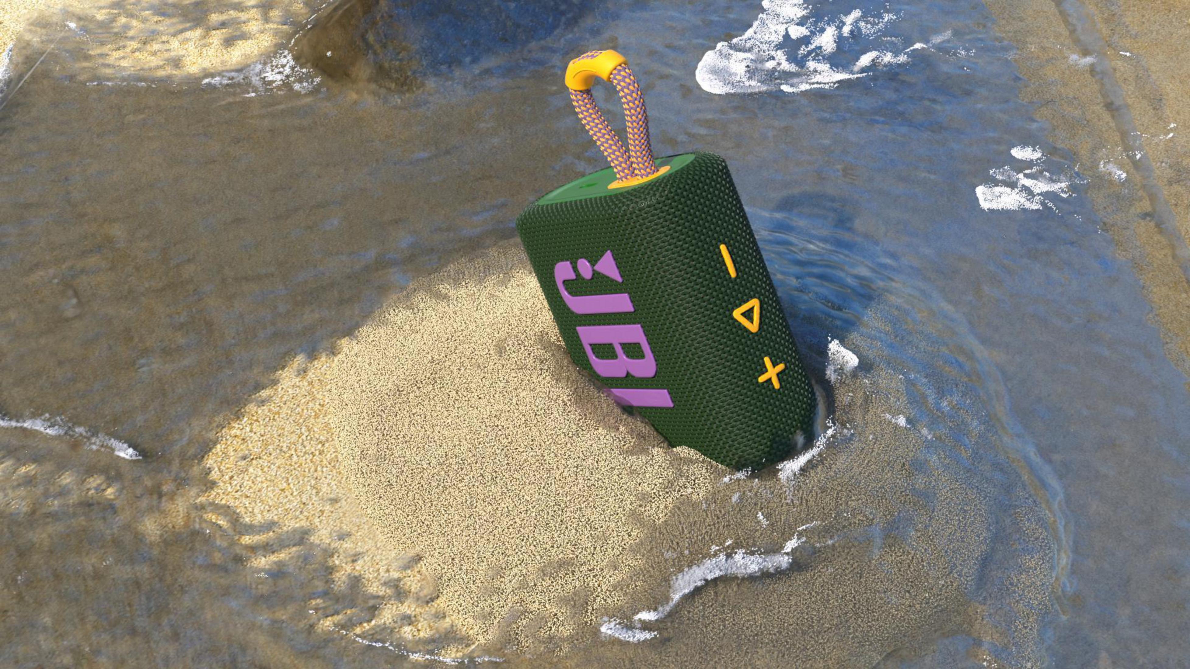 Zielony głośnik JBL w wodzie na piasku, z pomarańczowym uchwytem.