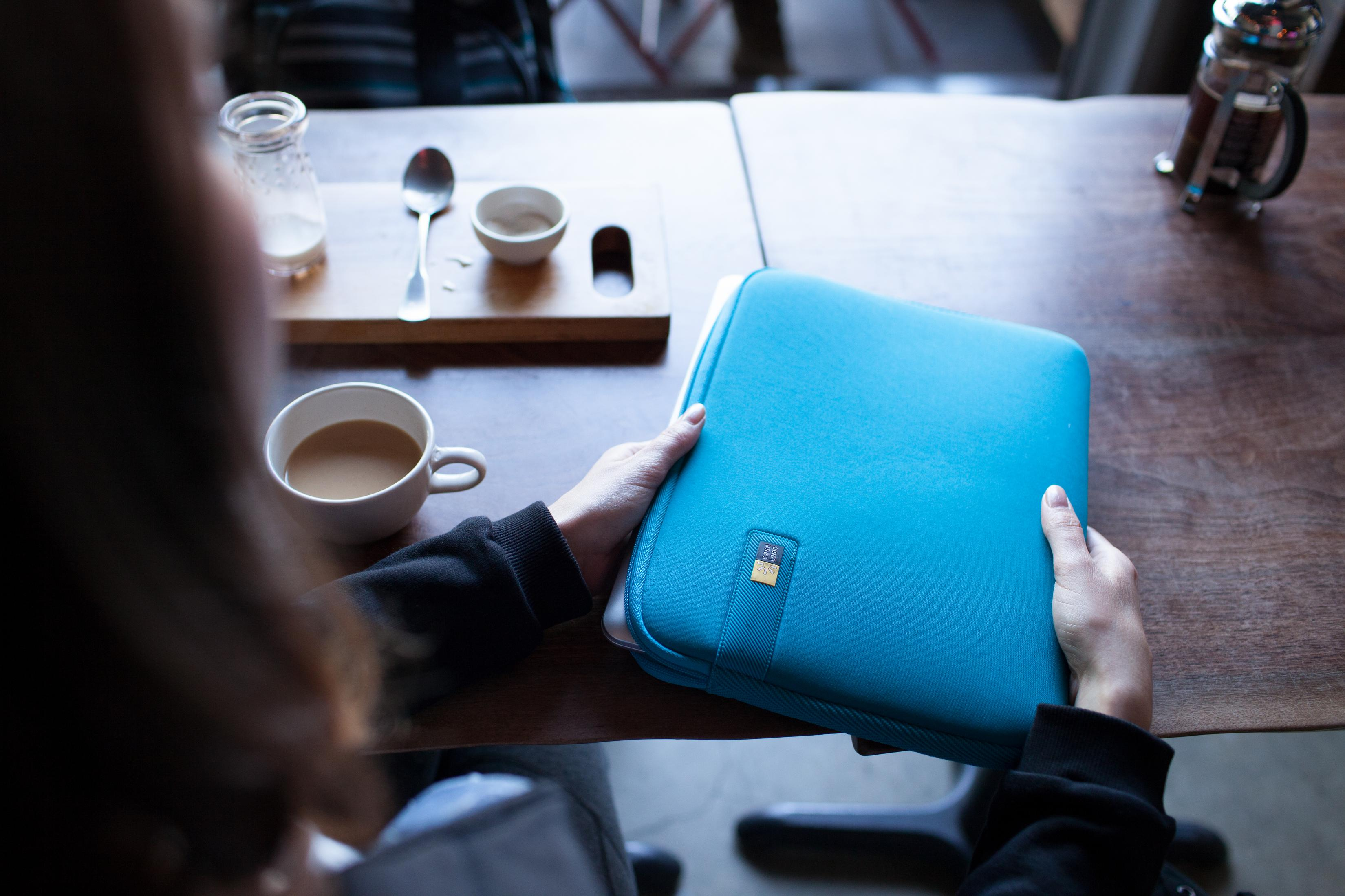 Person hält blaue Hülle auf Holztisch, mit Tasse und Löffel.