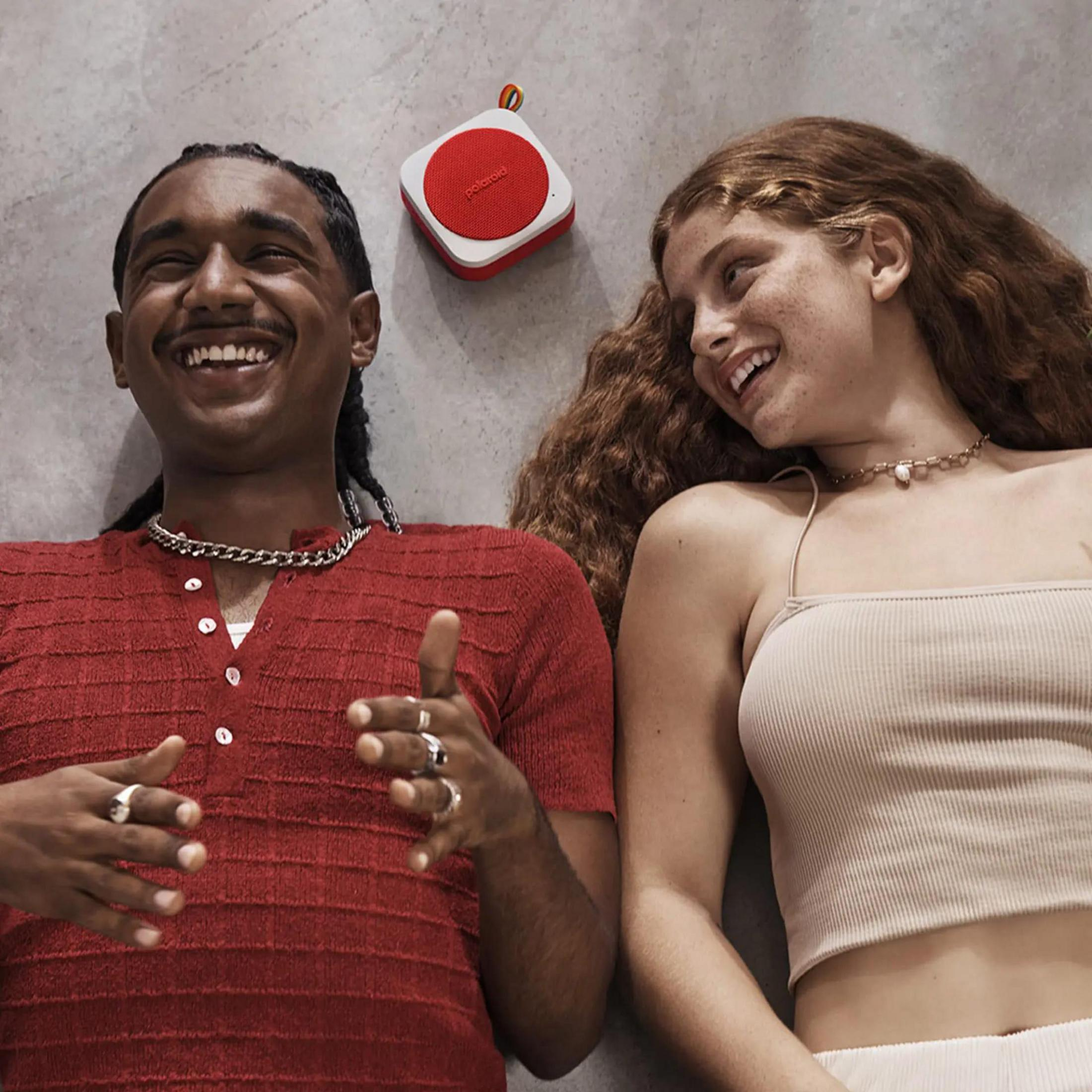 Dwie leżące osoby, uśmiechnięte, z czerwono-białym głośnikiem.