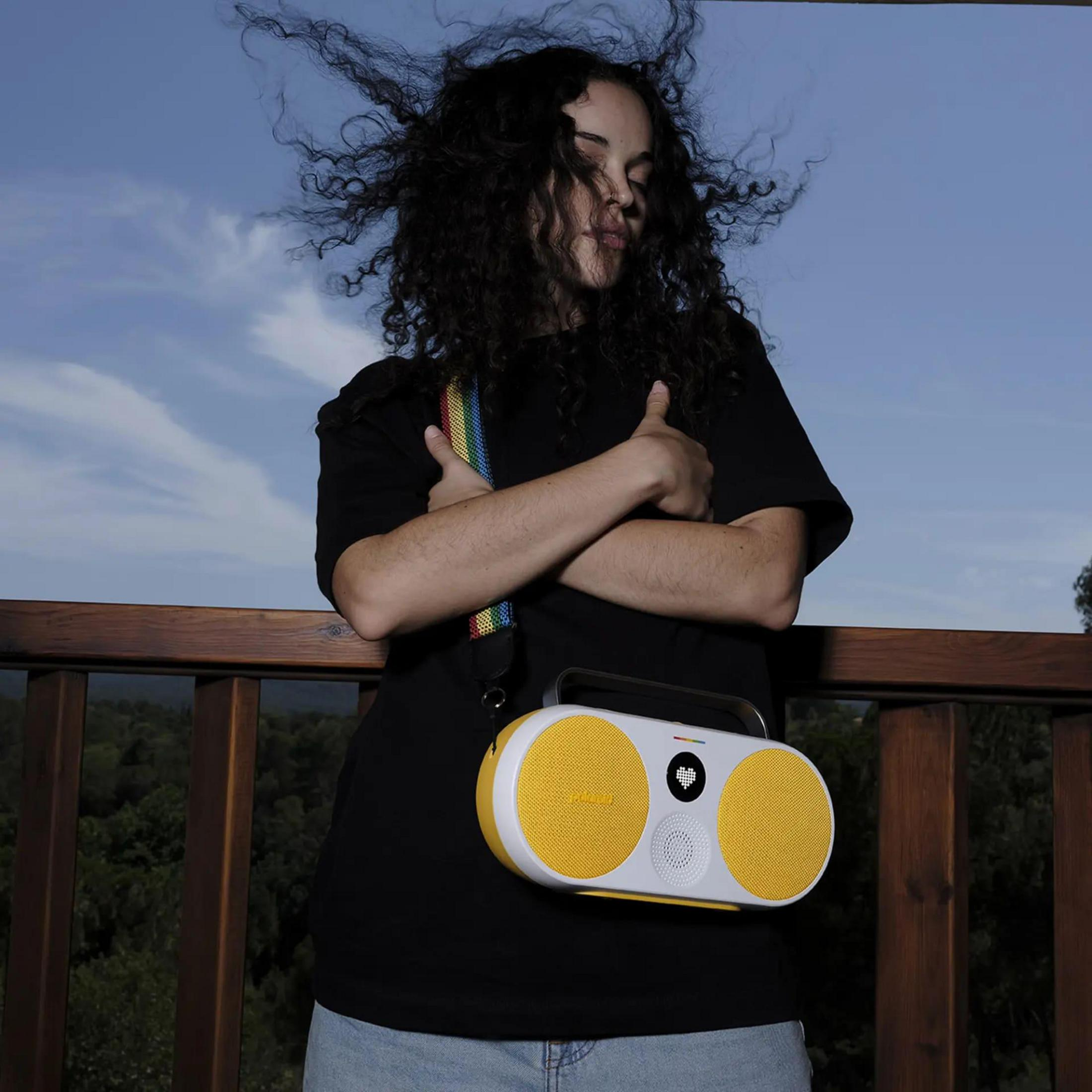 Kobieta z głośnikiem Marshall. Głośnik jest żółty i biały. Kobieta jest na tarasie.