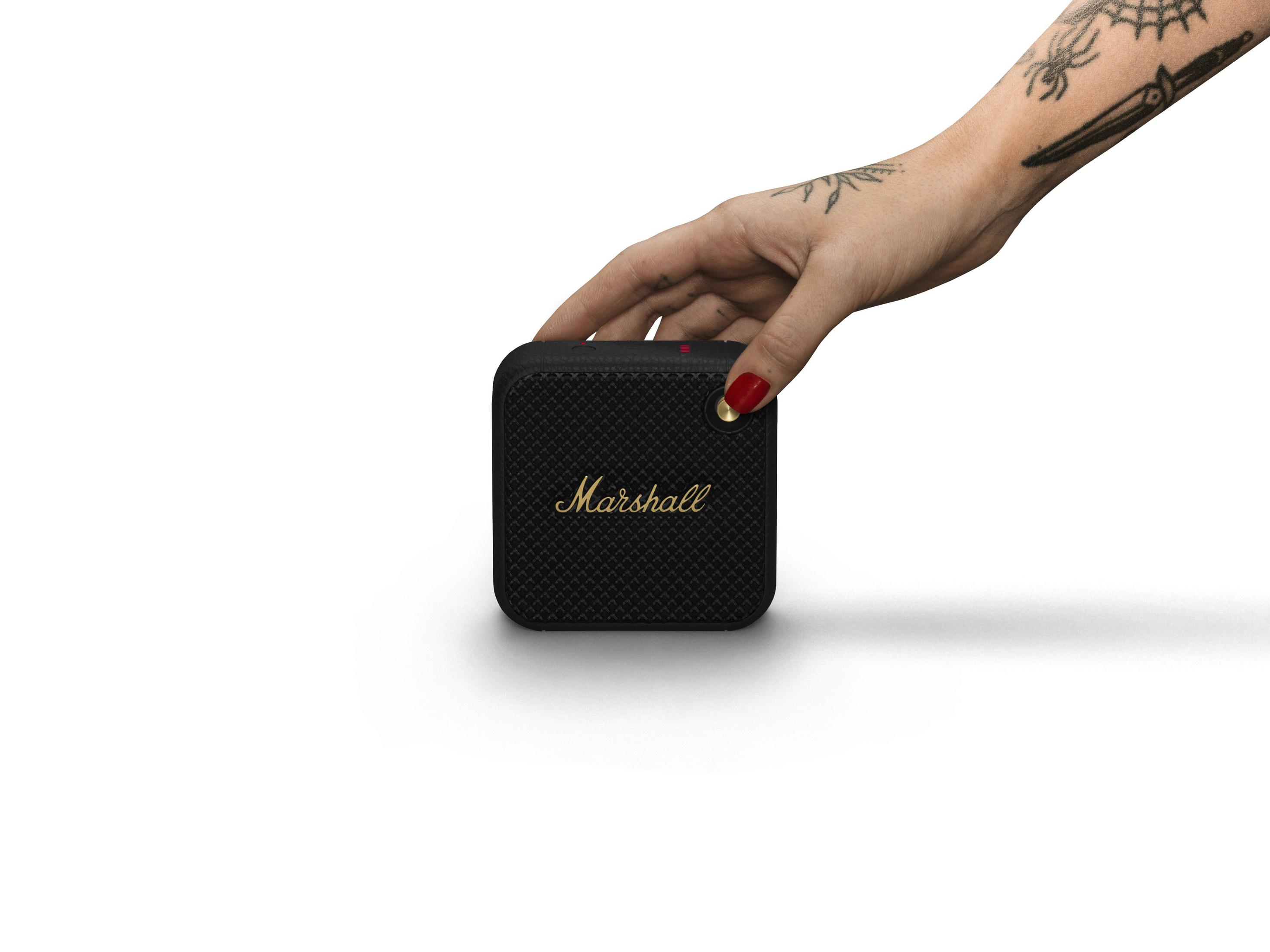 Mano che tiene un piccolo altoparlante Marshall nero con scritte dorate su sfondo bianco.
