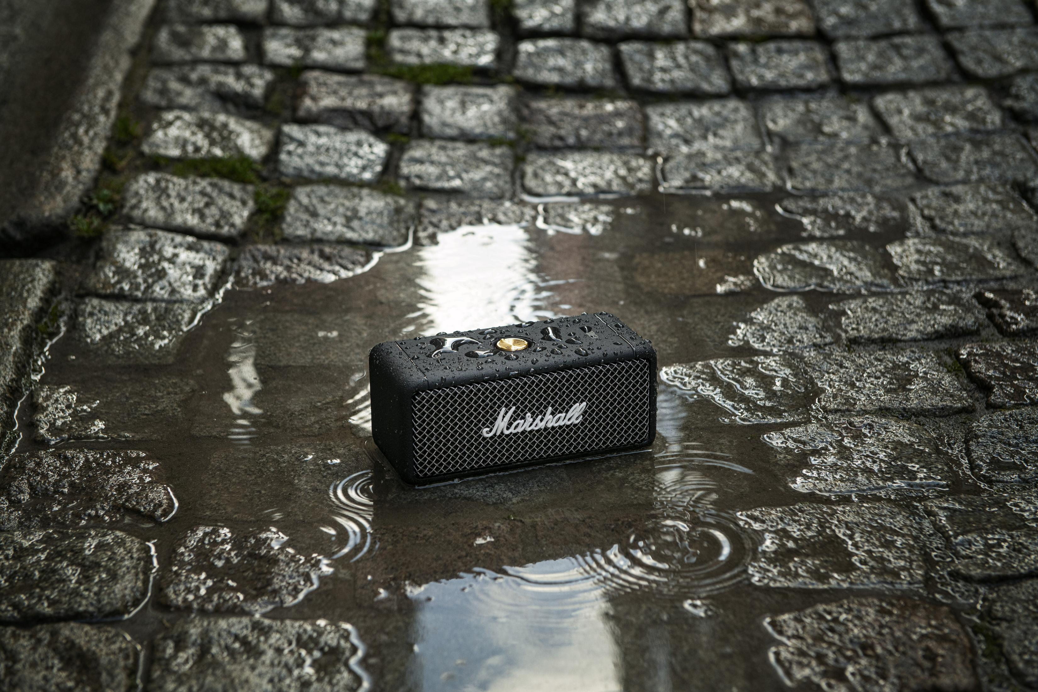 Schwarzer Marshall-Lautsprecher in einer Pfütze auf Kopfsteinpflaster. Wasser und Reflexionen.