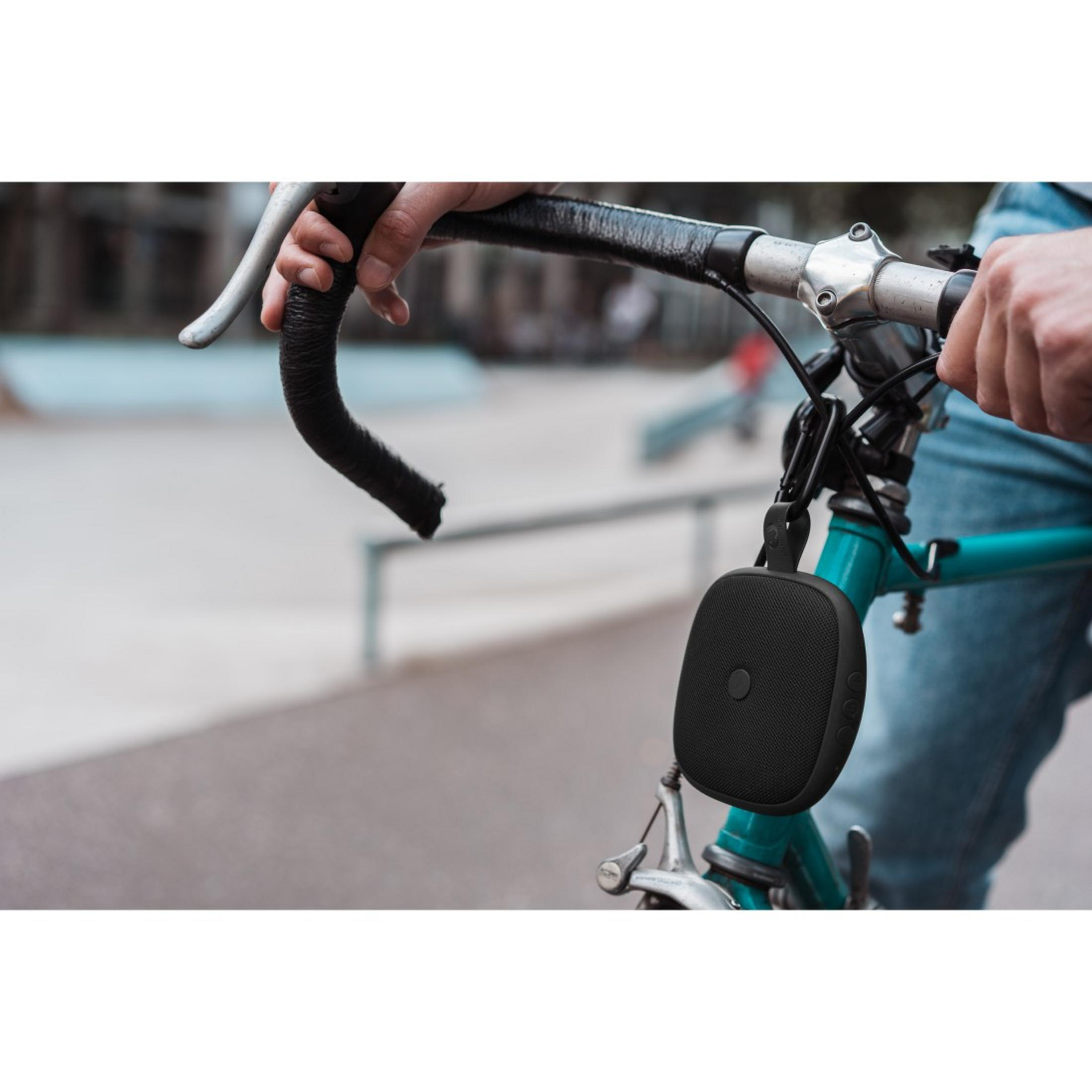 Czarny głośnik zamontowany na rowerze, trzymany przez czyjąś dłoń.
