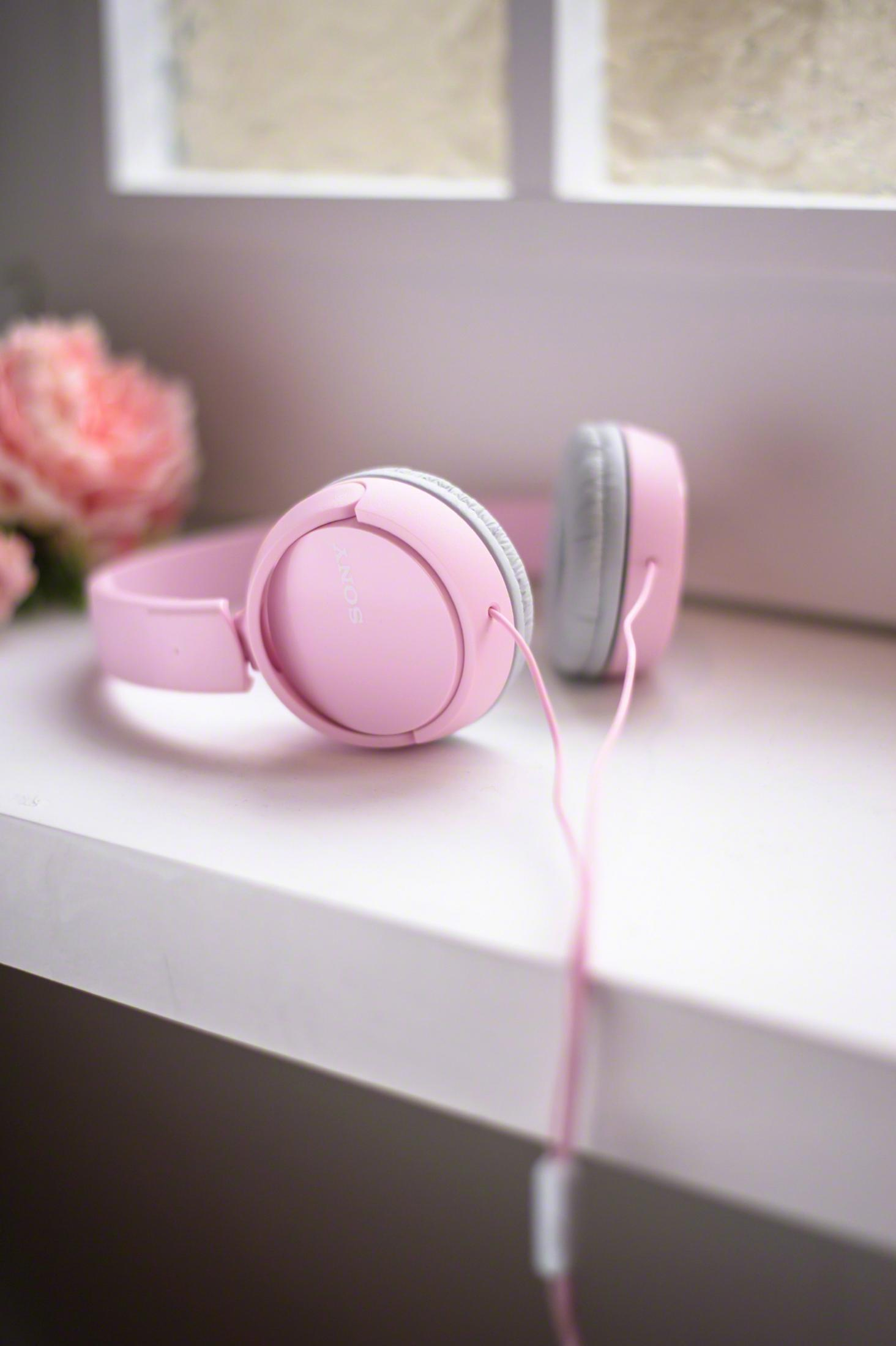 Cuffie Sony rosa su una superficie bianca con finestra e fiori sullo sfondo.