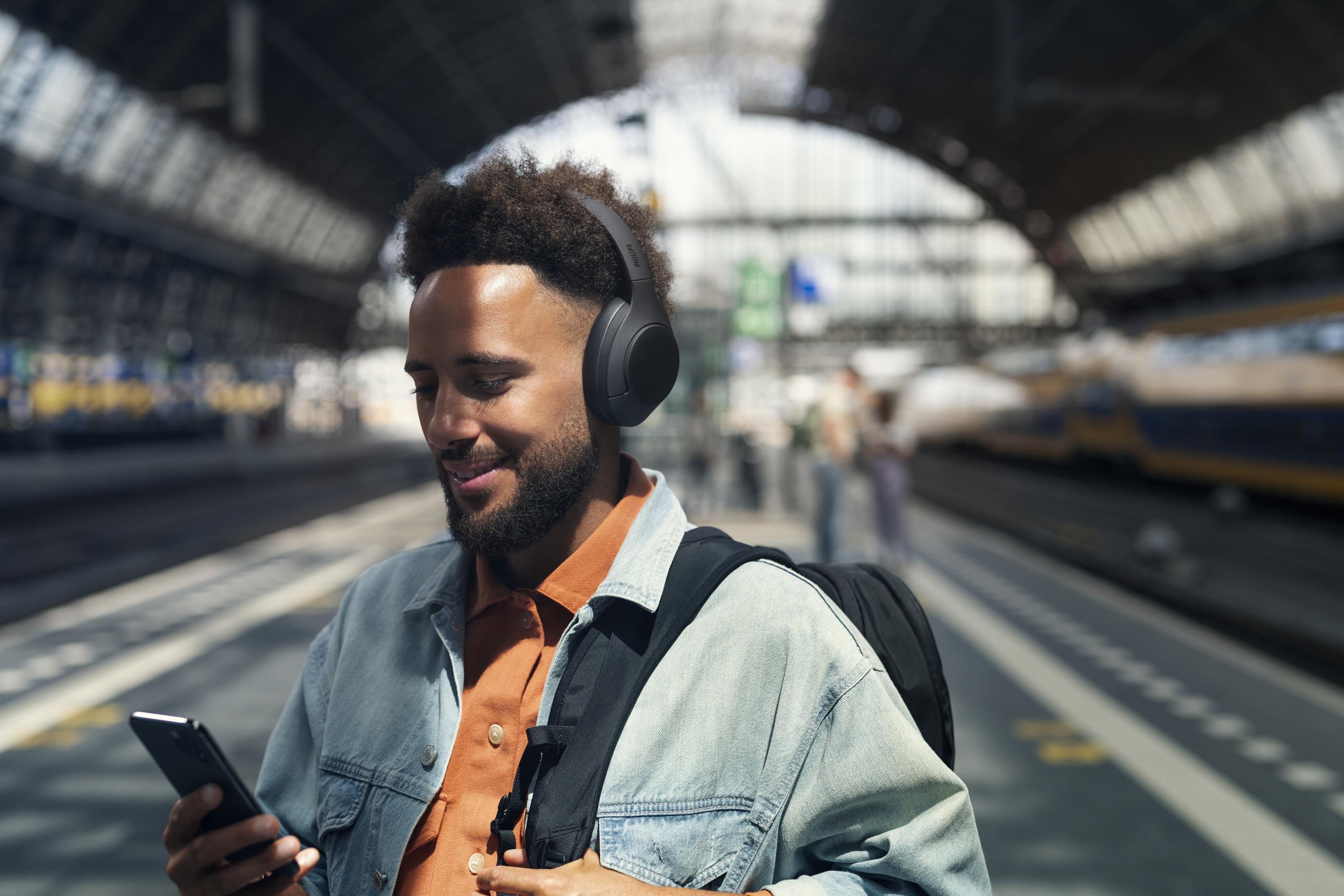 Ein Mann am Bahnhof mit Kopfhörern, der auf ein Telefon schaut.