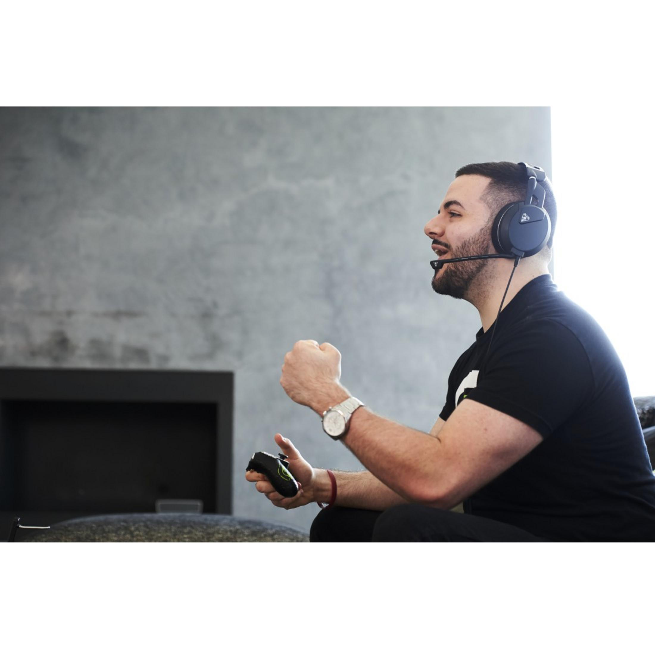 Mężczyzna w zestawie słuchawkowym, gra w grę wideo, zaciska pięść. Szara ściana w tle.