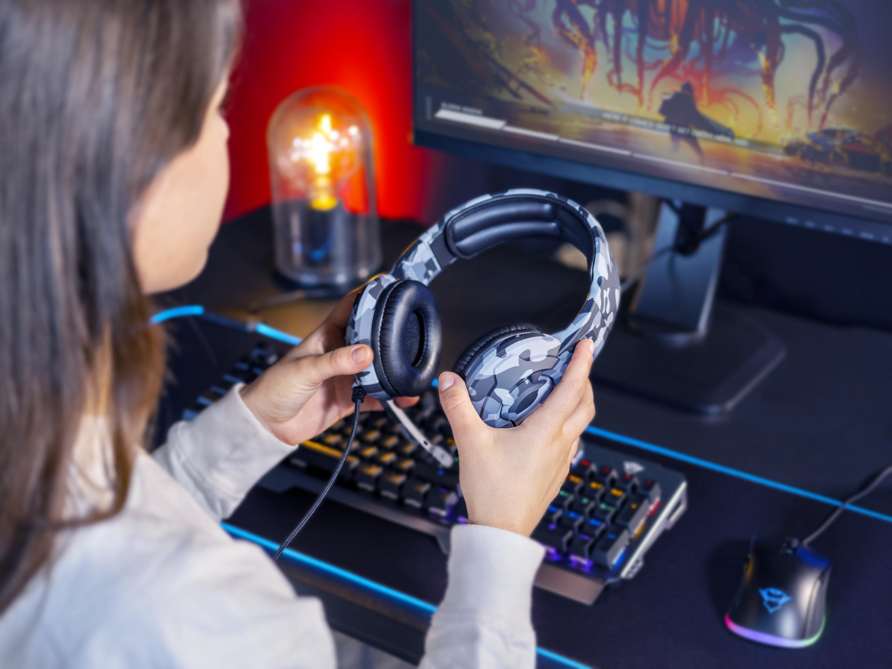 Kobieta trzymająca słuchawki moro w pobliżu klawiatury i monitora z świecącym światłem.