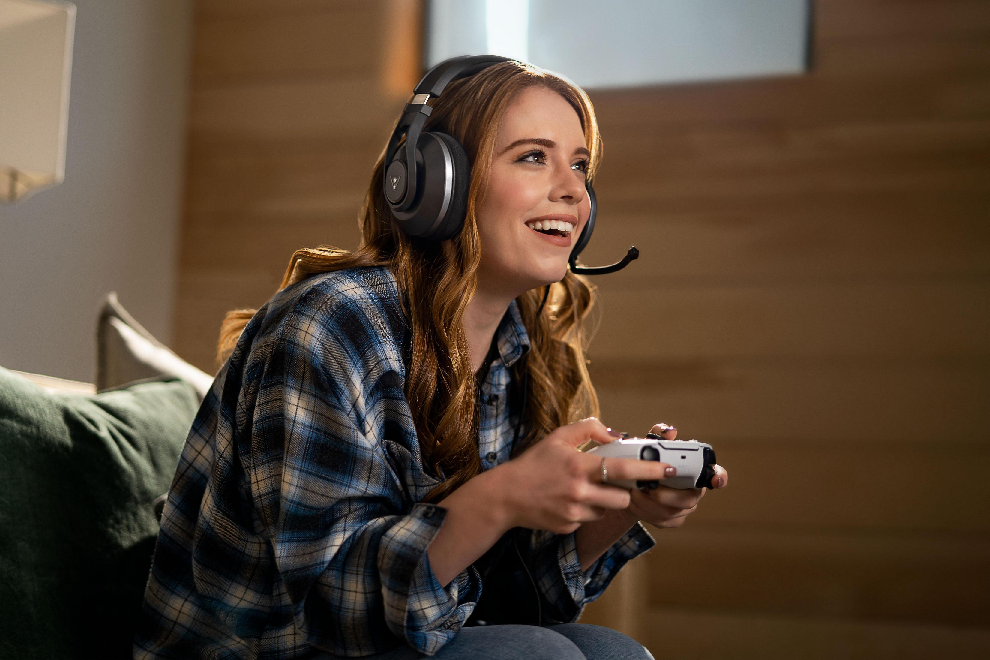 Donna con cuffie, gioca a un videogioco con un controller. Sta sorridendo.