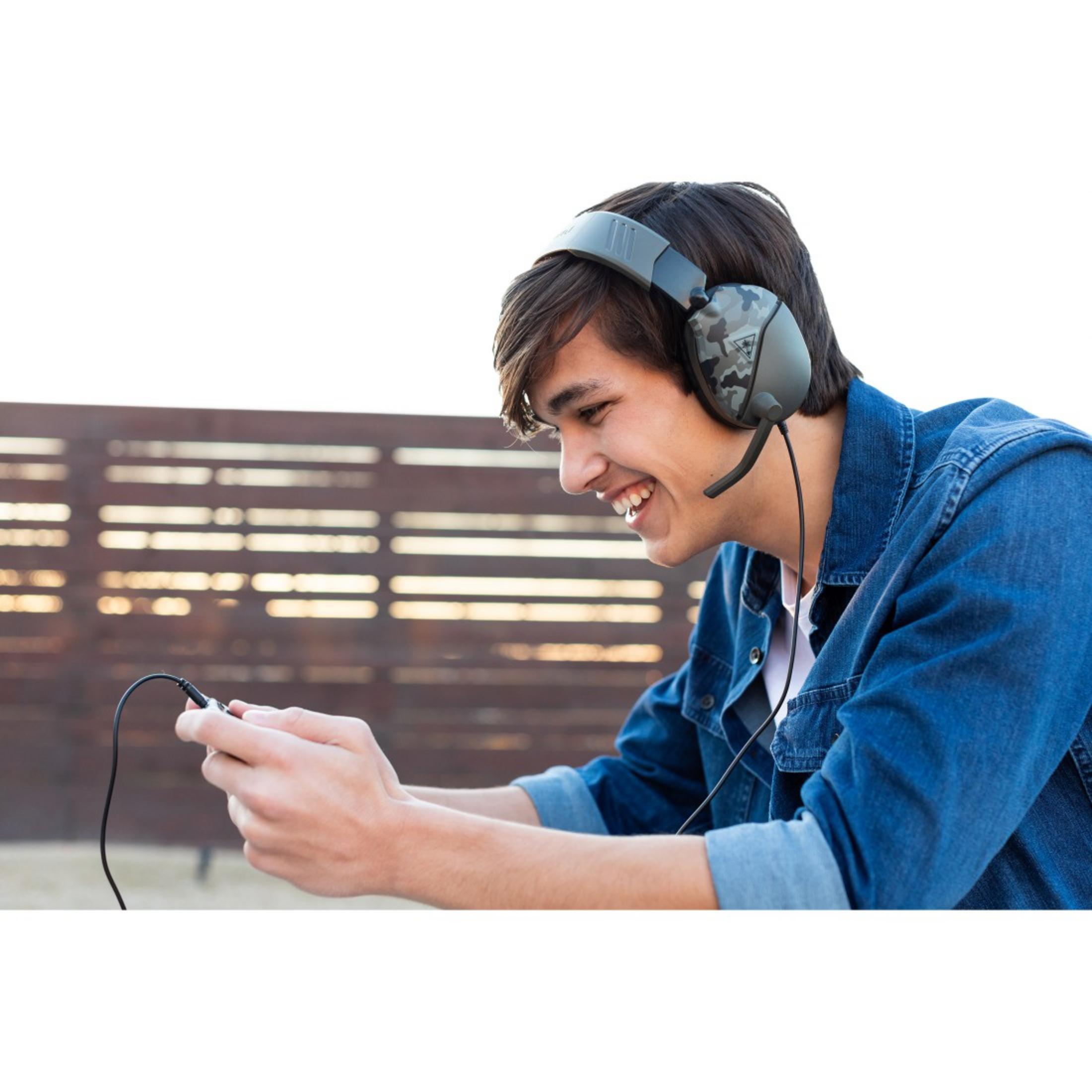 Młody mężczyzna uśmiecha się, grając w grę na smartfonie, w słuchawkach.