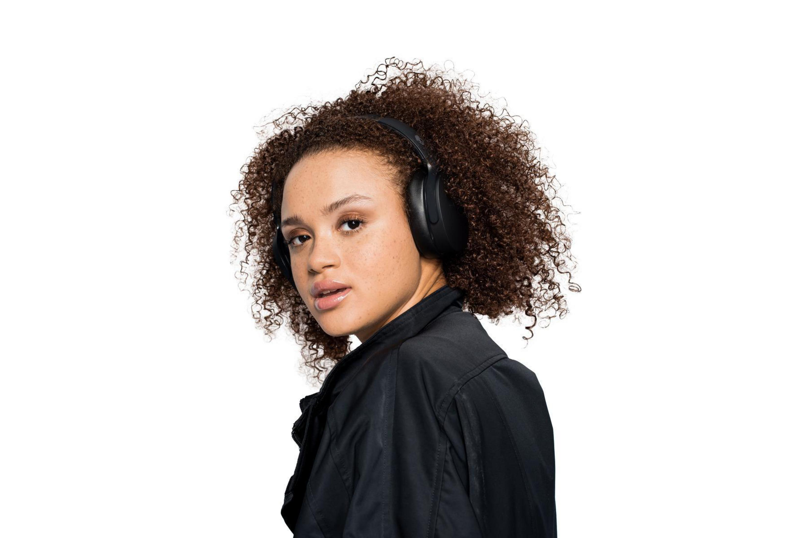 Kobieta z kręconymi włosami w słuchawkach, patrzy w kamerę.
