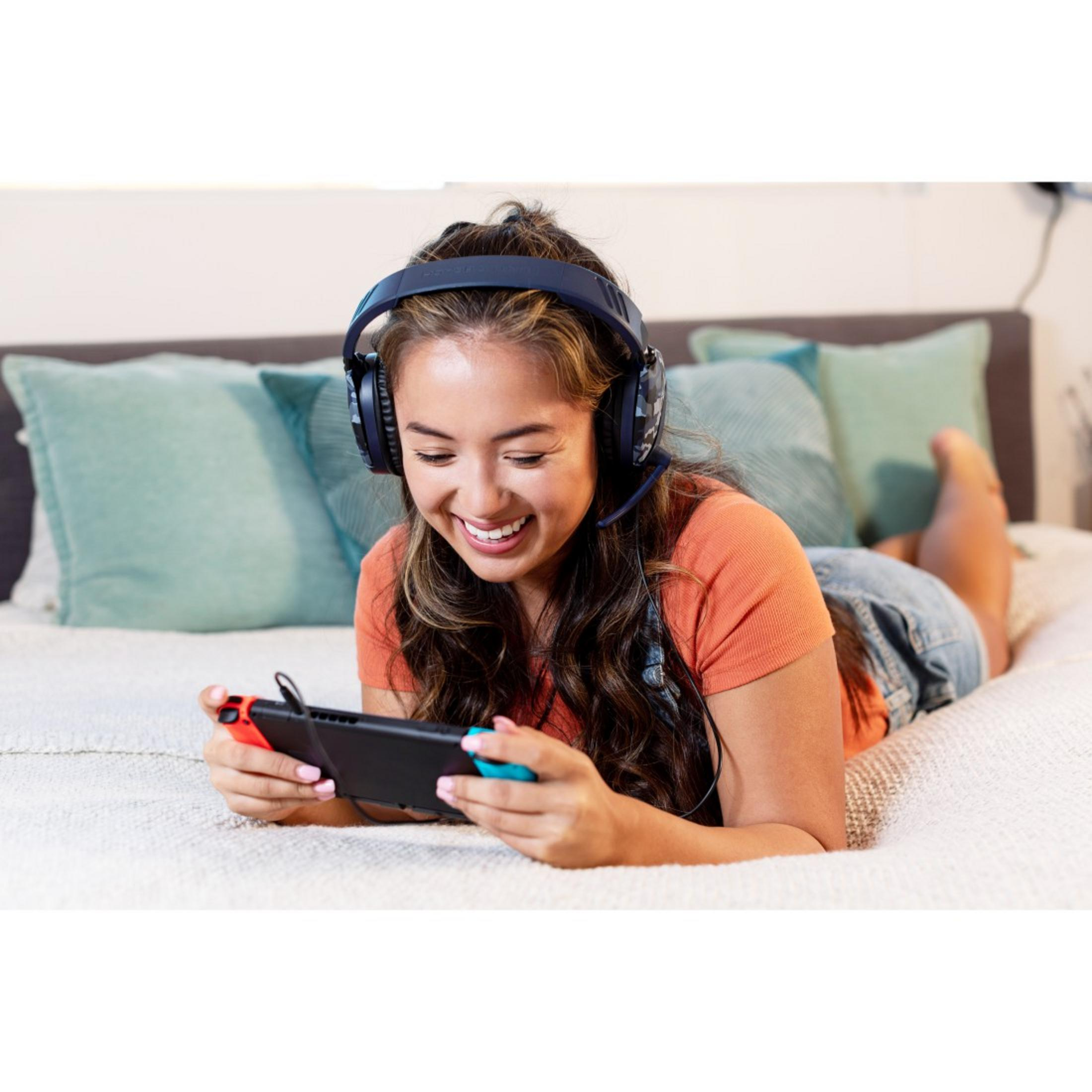 Młoda kobieta w słuchawkach i szortach dżinsowych gra w grę na łóżku.