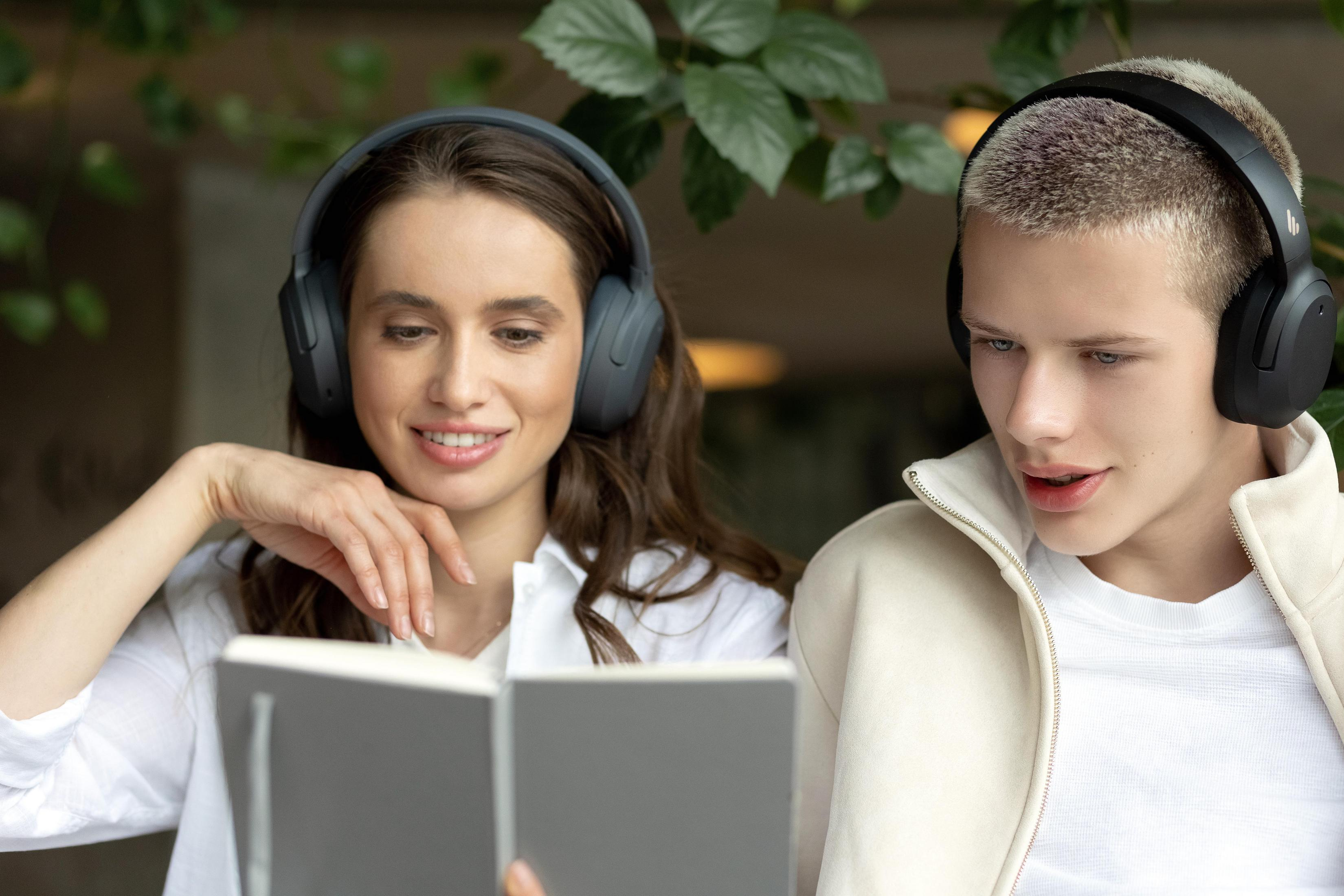 Dwie osoby ze słuchawkami przeglądają książkę. Jedna się uśmiecha.