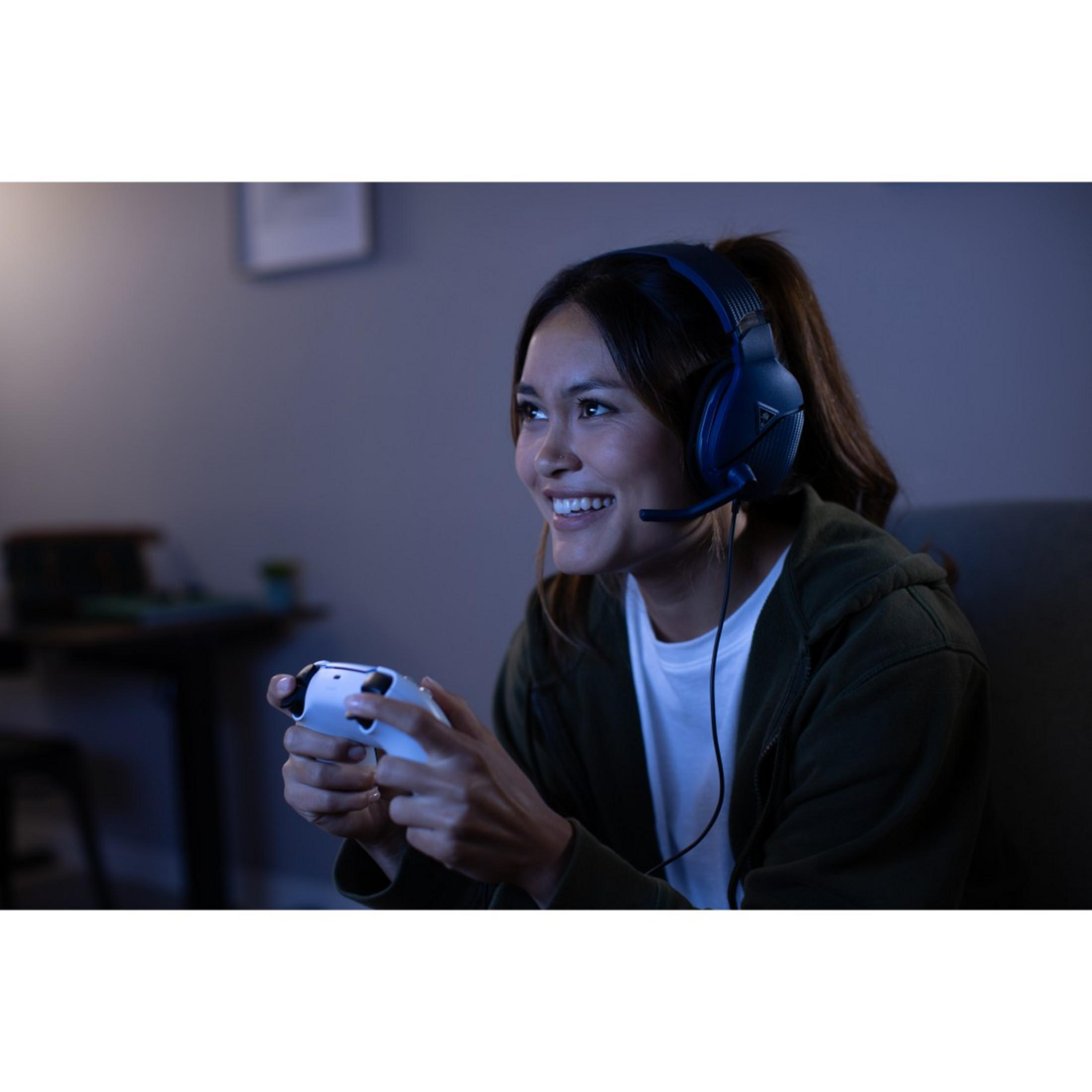 Kobieta uśmiechnięta podczas gry, nosząca niebieski zestaw słuchawkowy i trzymająca kontroler do gier.