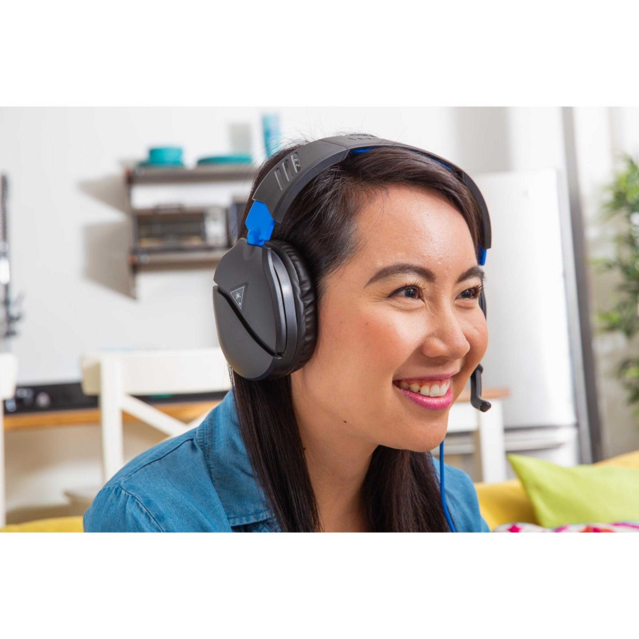 Kobieta w słuchawkach uśmiecha się. W tle biała lodówka i kanapa.