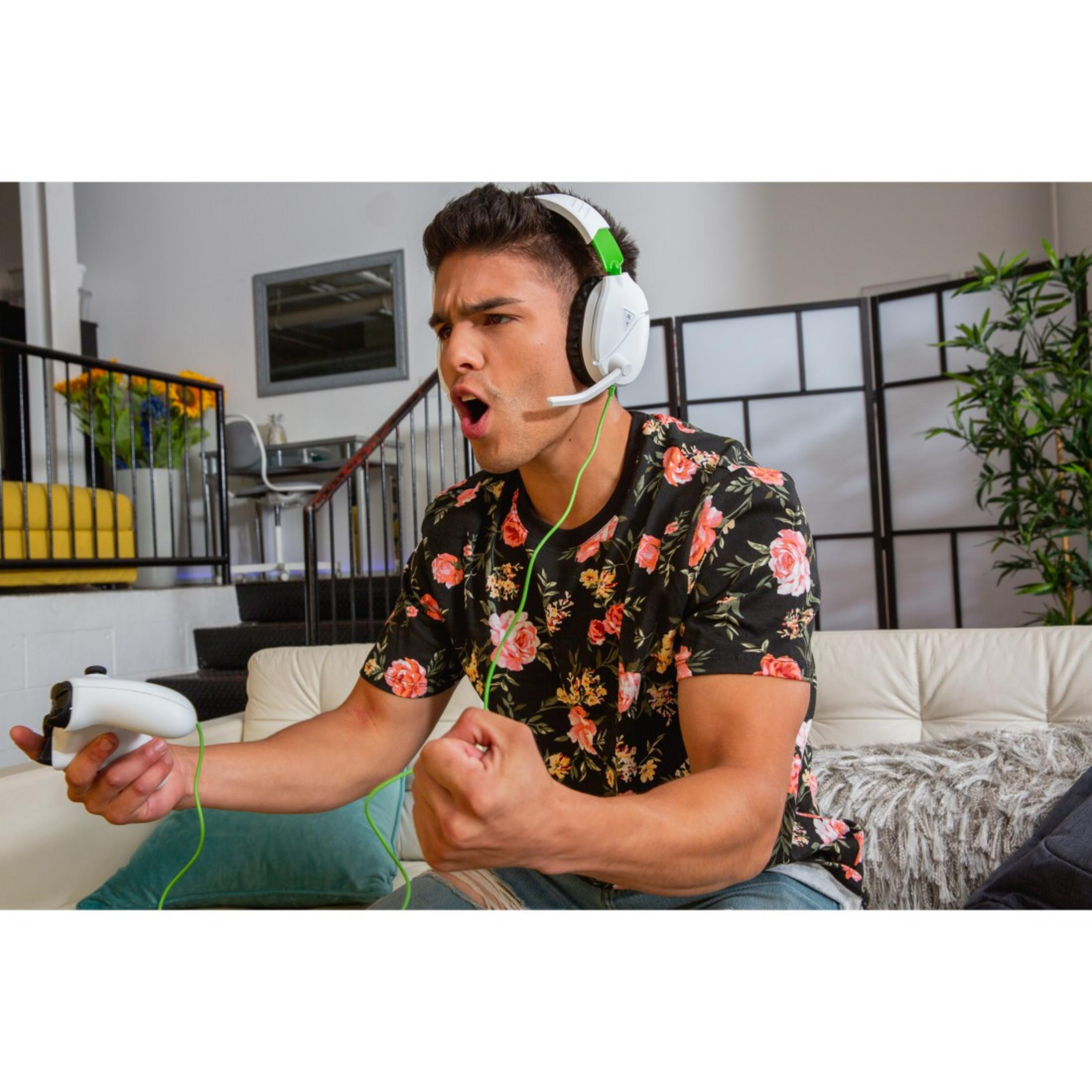 Hombre jugando videojuego, con auriculares. Está emocionado y sostiene un mando blanco.