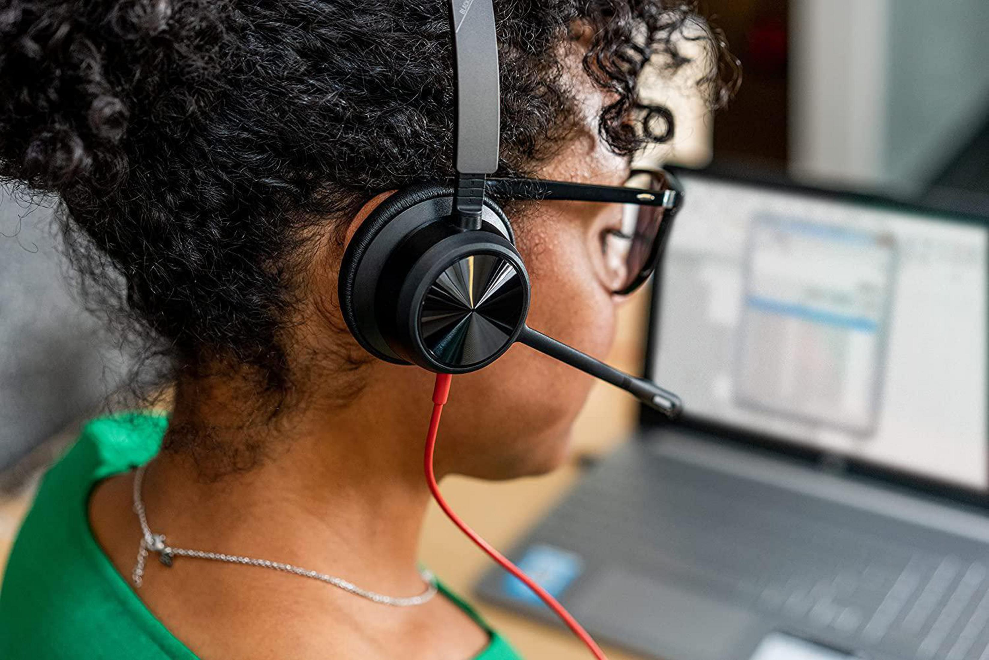 Kobieta w okularach i czarnym zestawie słuchawkowym z mikrofonem, pracująca na laptopie.