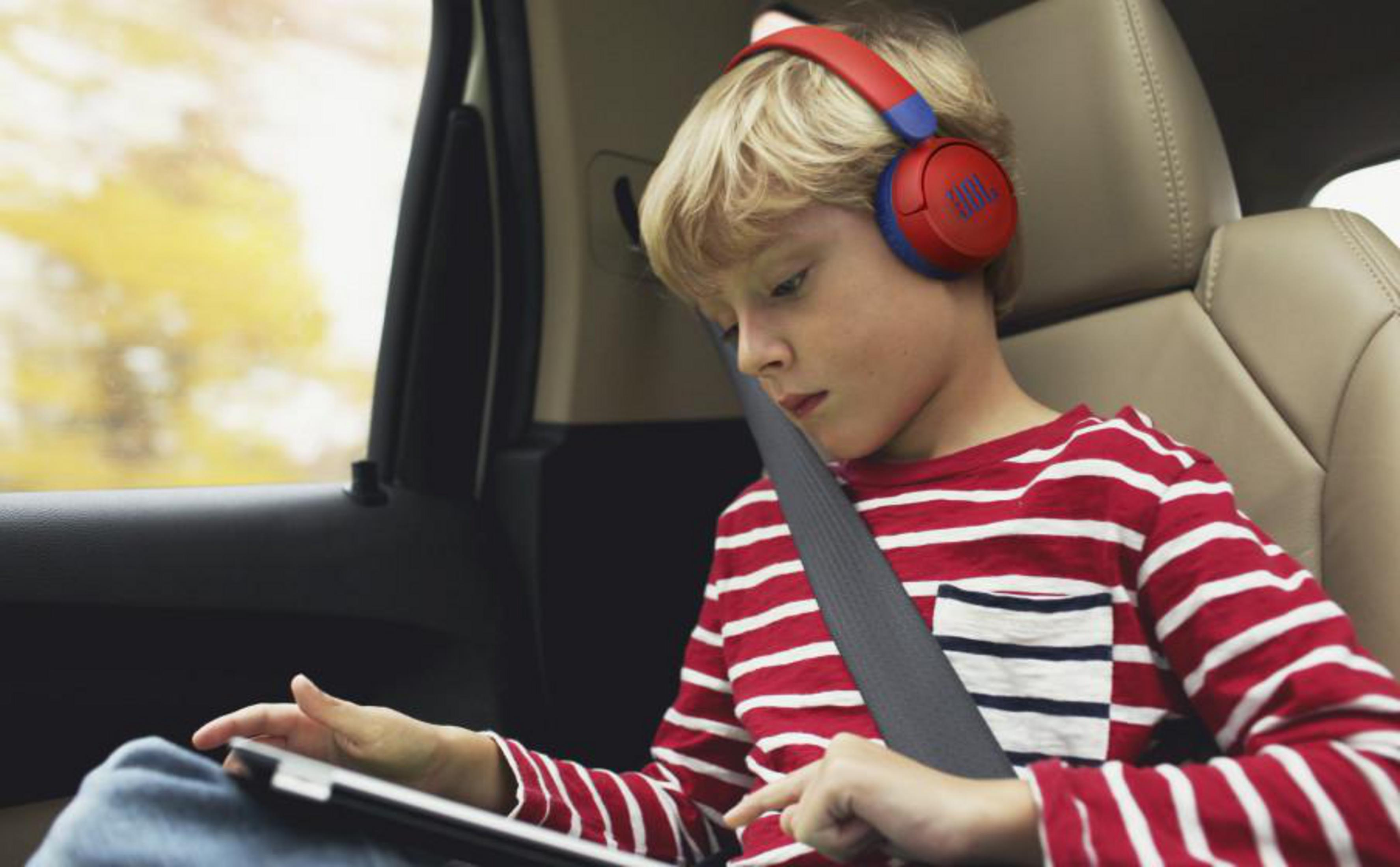 Un niño con auriculares en un coche mira una tableta mientras usa el cinturón de seguridad.