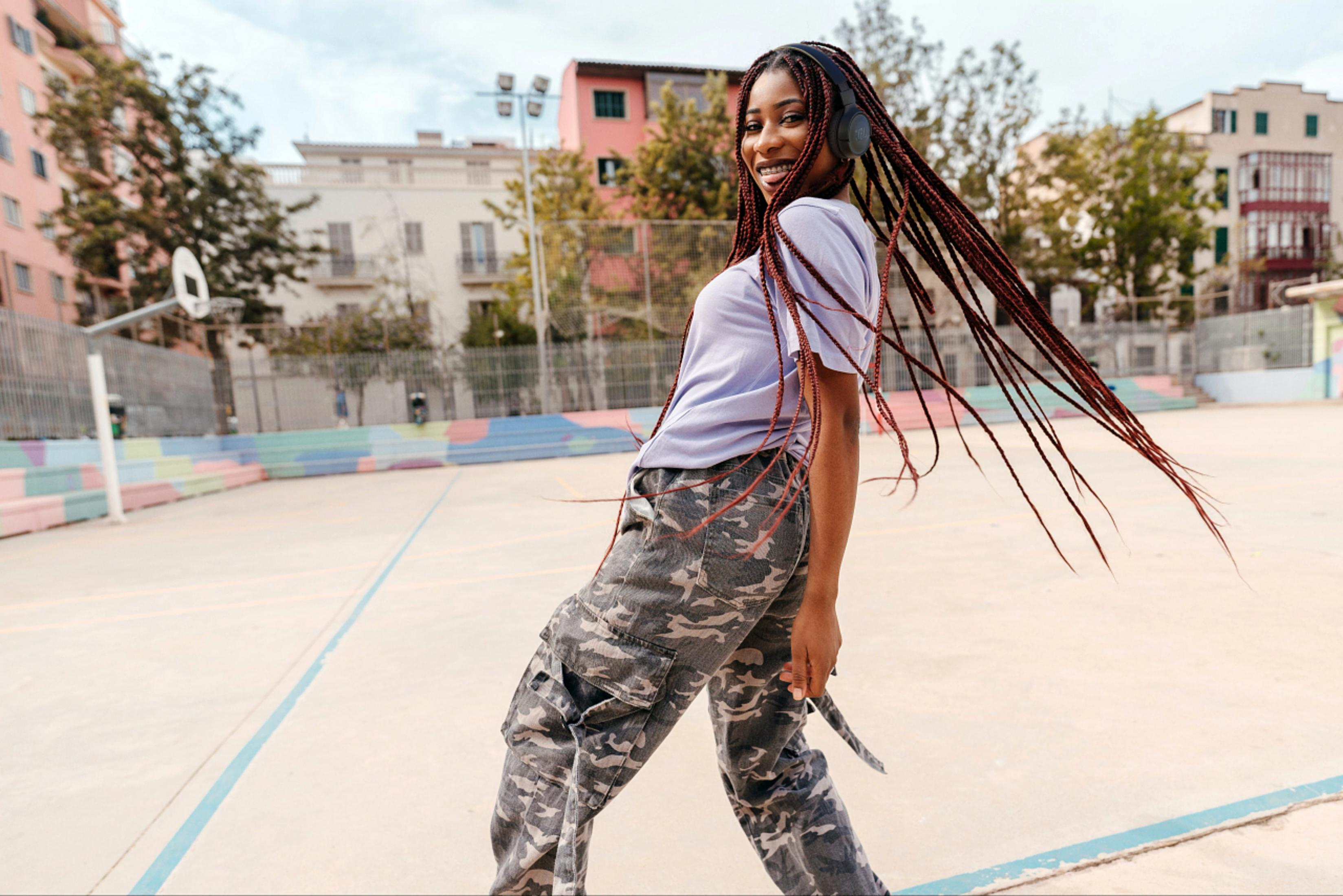 Kobieta w spodniach moro i słuchawkach uśmiechająca się na tle kolorowego tła.