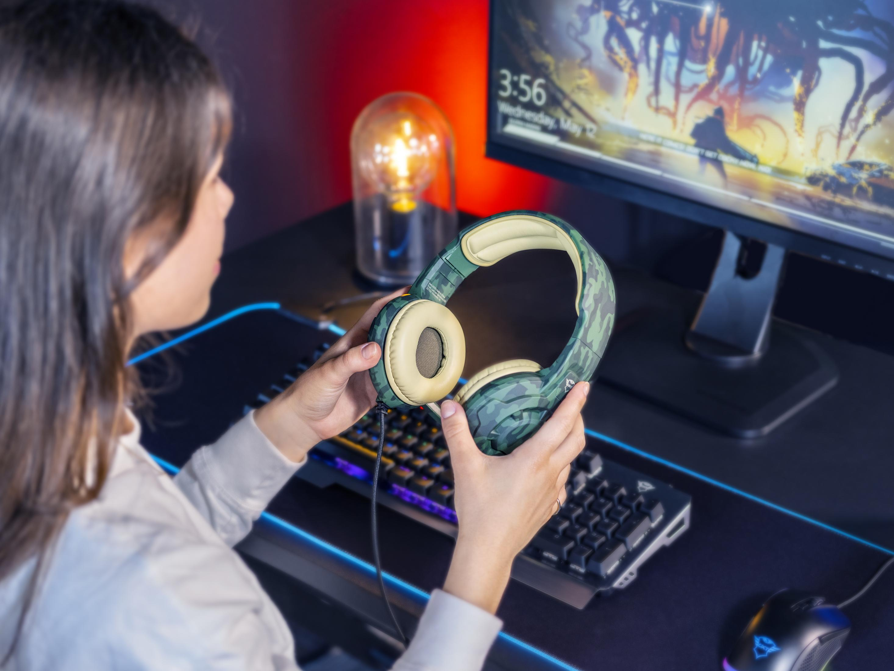 Una donna che tiene un headset da gaming mimetico vicino a un computer con un'impostazione di gioco.
