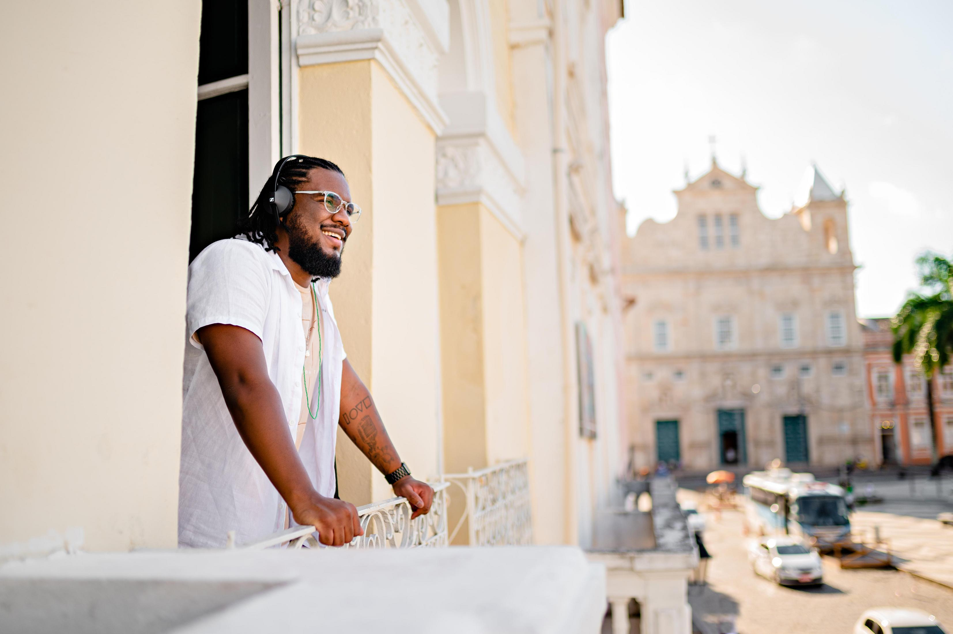 Un homme sur un balcon, portant un casque, regardant vers un bâtiment. Il sourit.