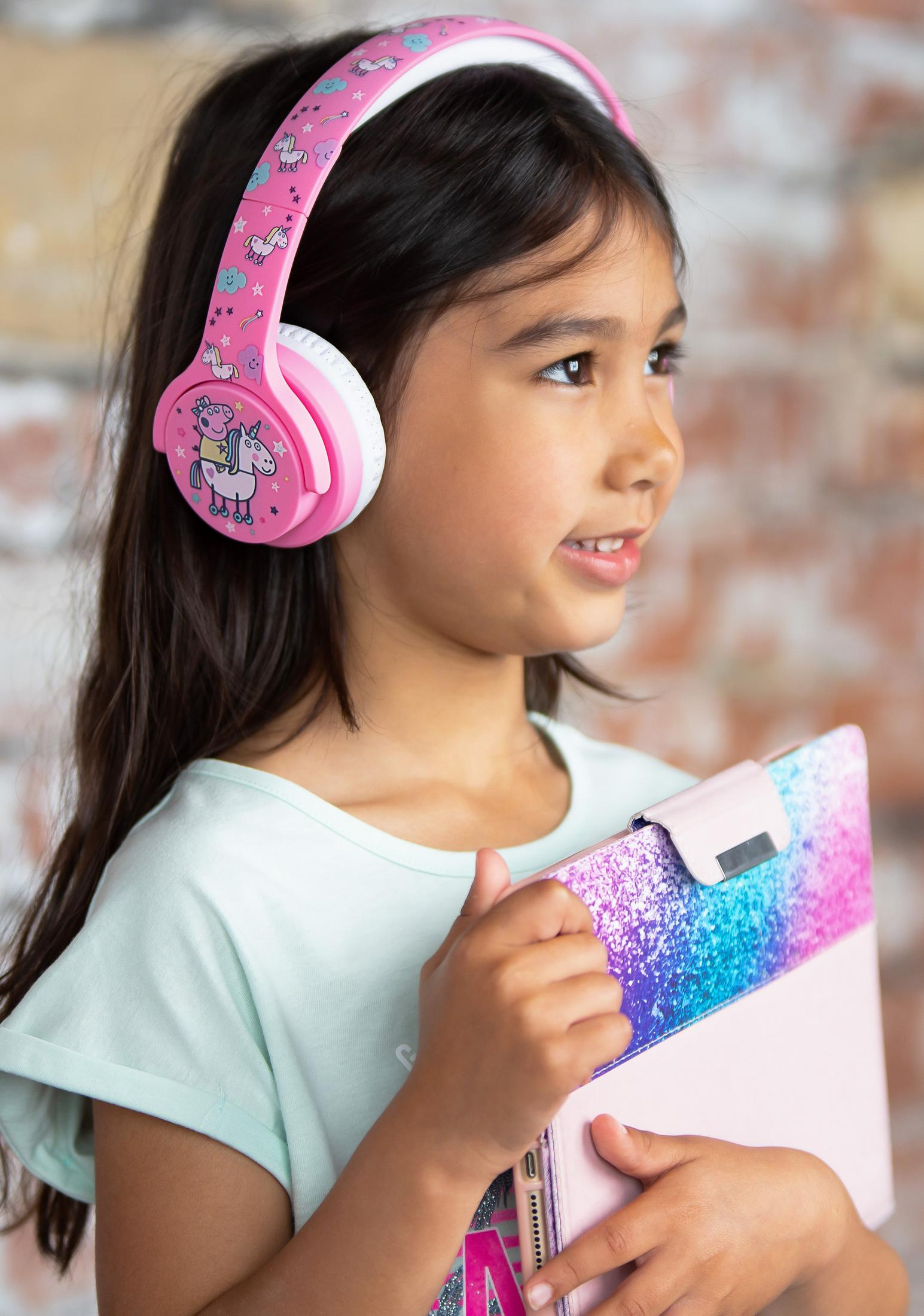 Una niña con auriculares rosas sosteniendo una tableta.