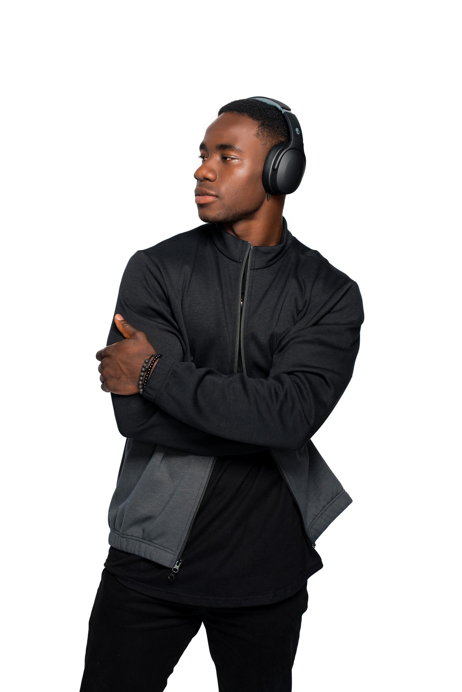 Mężczyzna w czarnej kurtce, czarnej koszuli i czarnych spodniach ze słuchawkami.