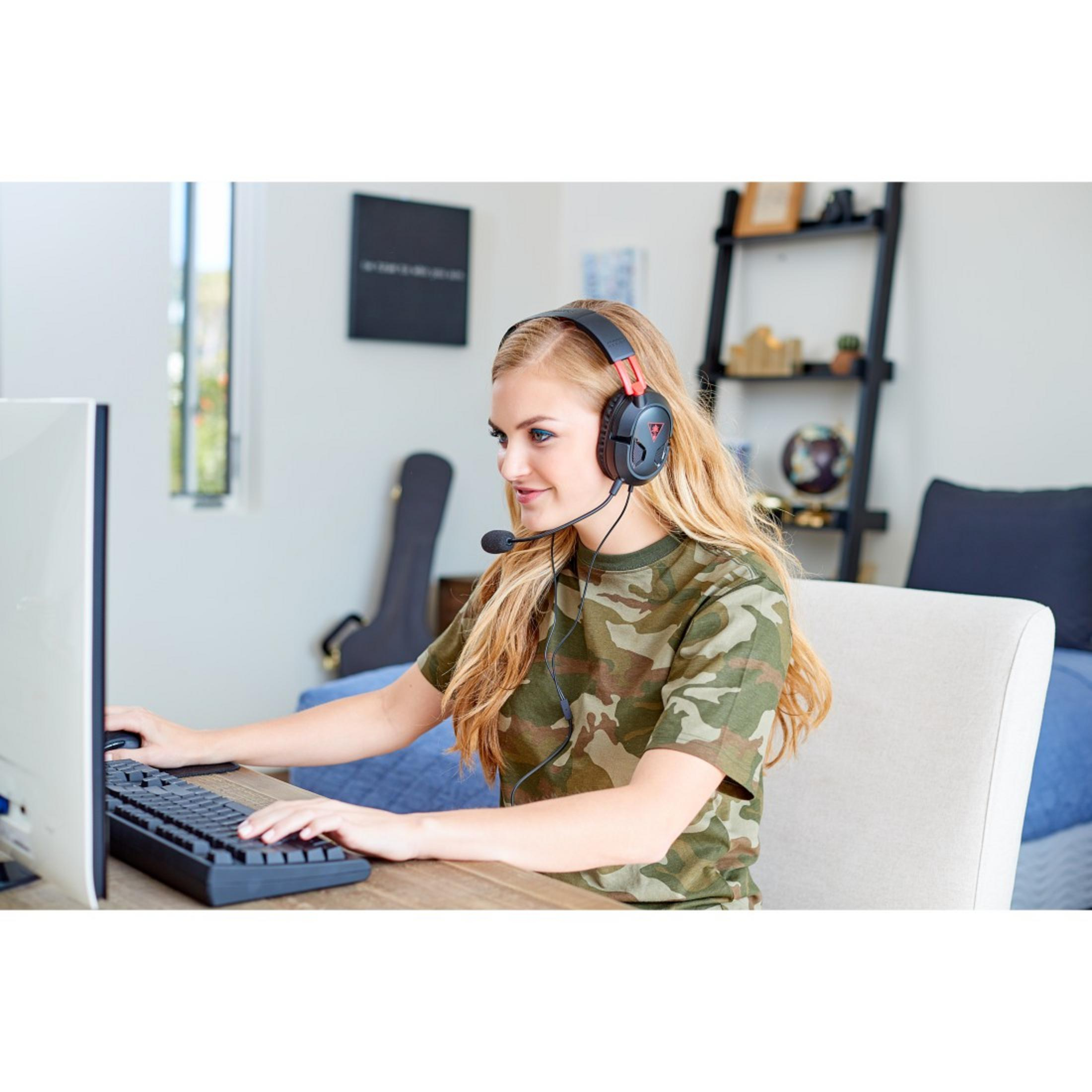 Une femme portant un casque de jeu utilise un ordinateur. Elle est devant un écran.