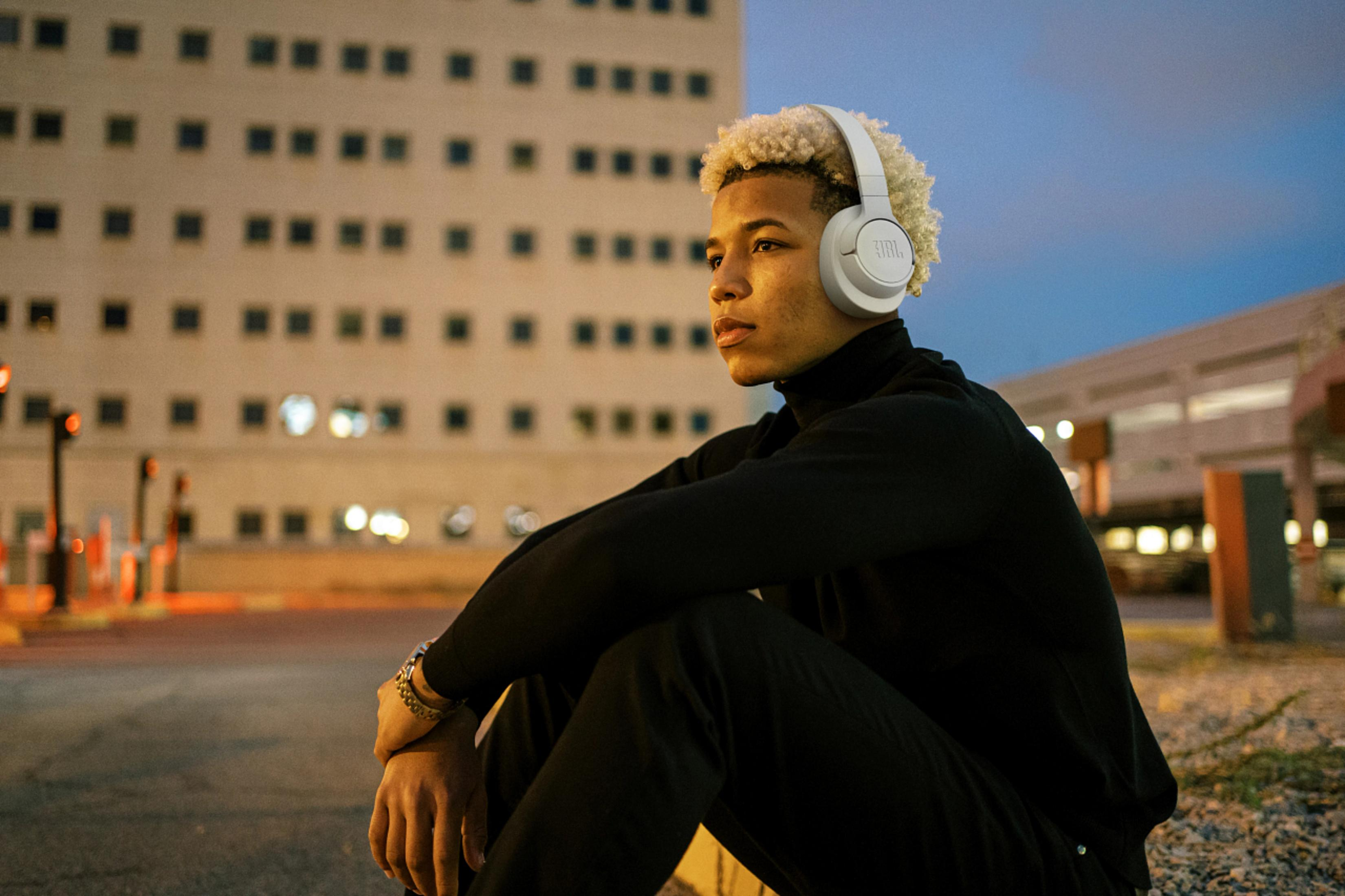 Mężczyzna w białych słuchawkach siedzący na zewnątrz w pobliżu budynku.