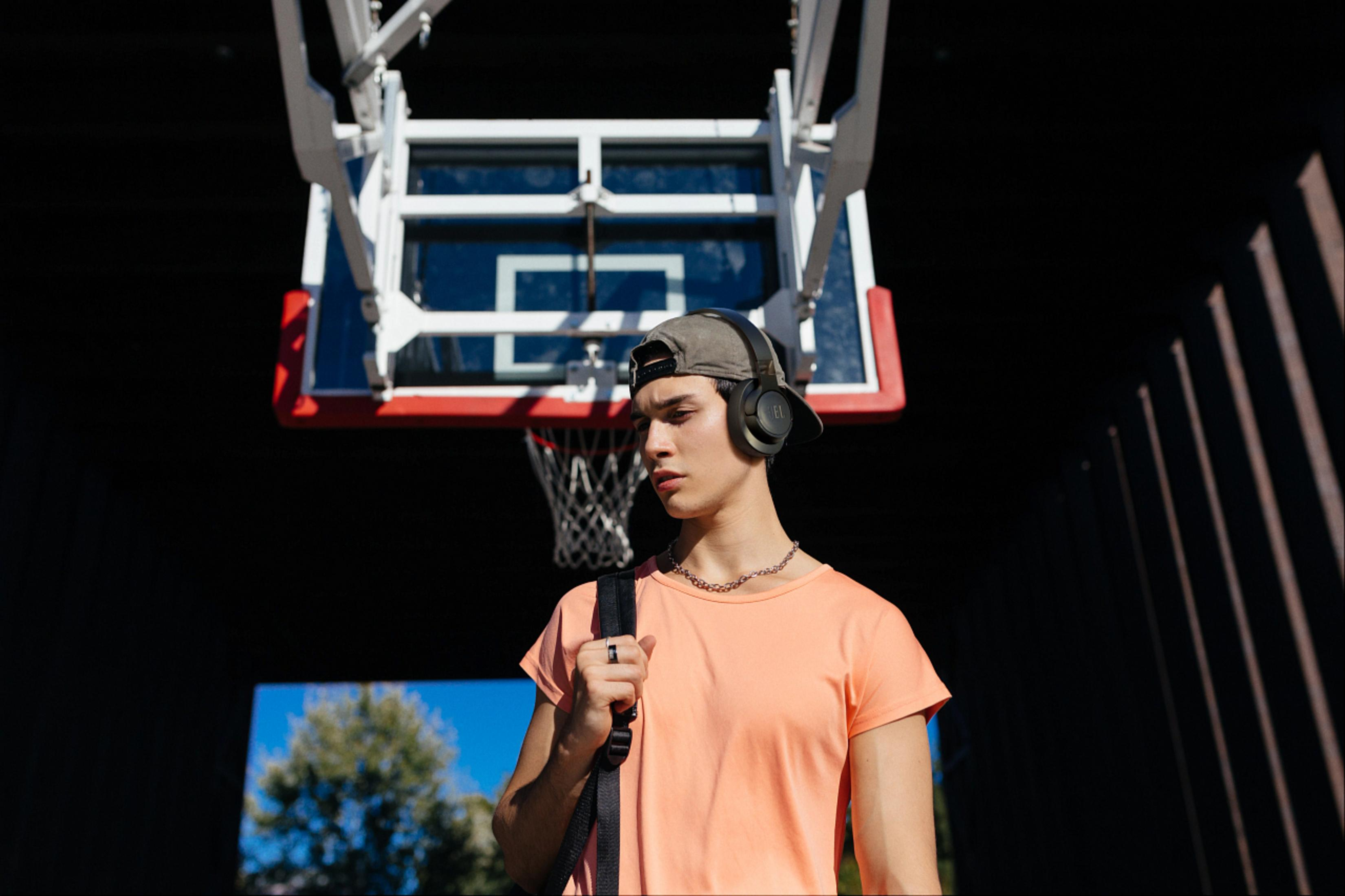 Mężczyzna w czapce i słuchawkach na boisku do koszykówki. Trzyma torbę.