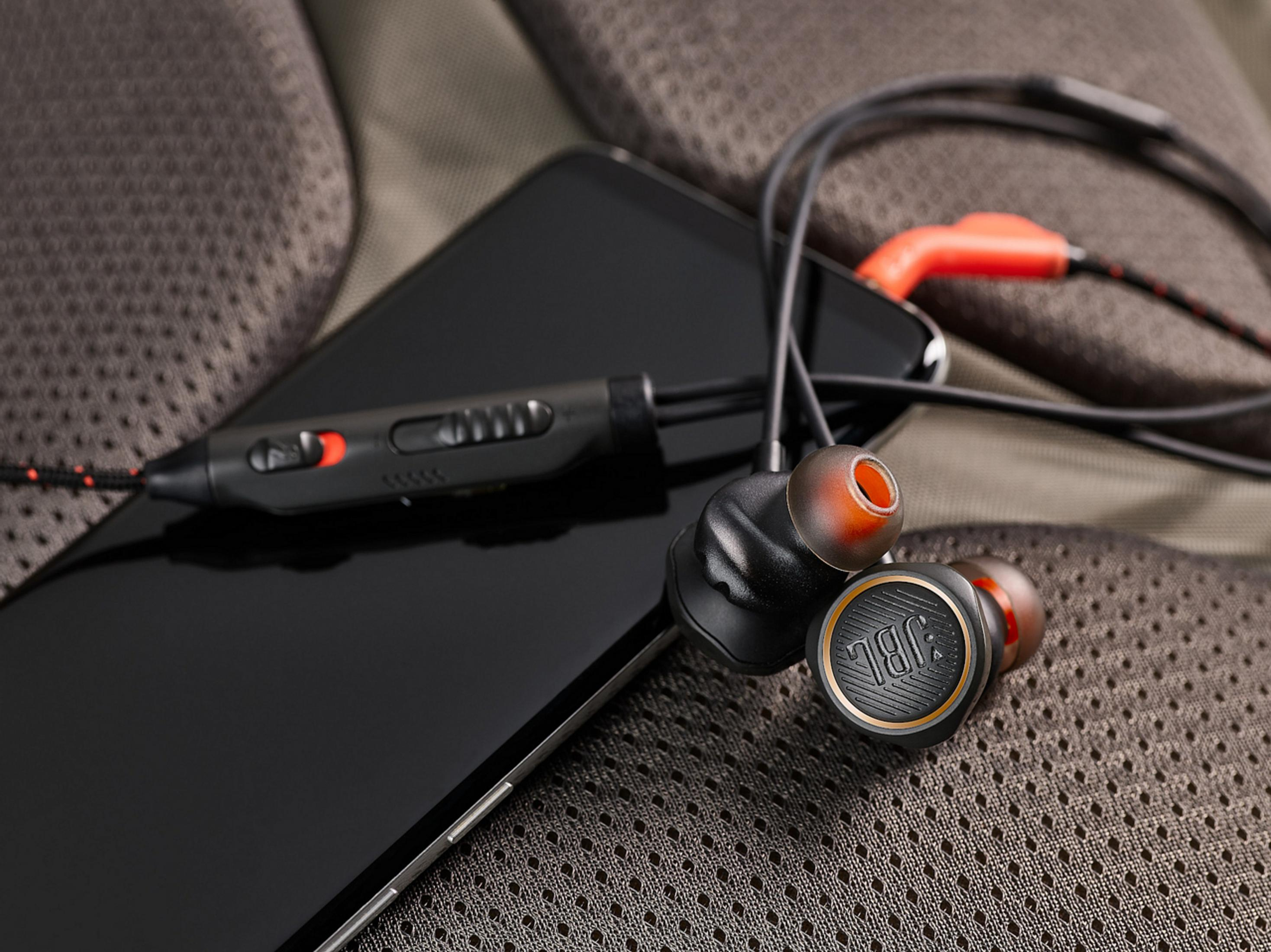 Smartphone negro con auriculares negros y naranjas. El teléfono está sobre una superficie gris.
