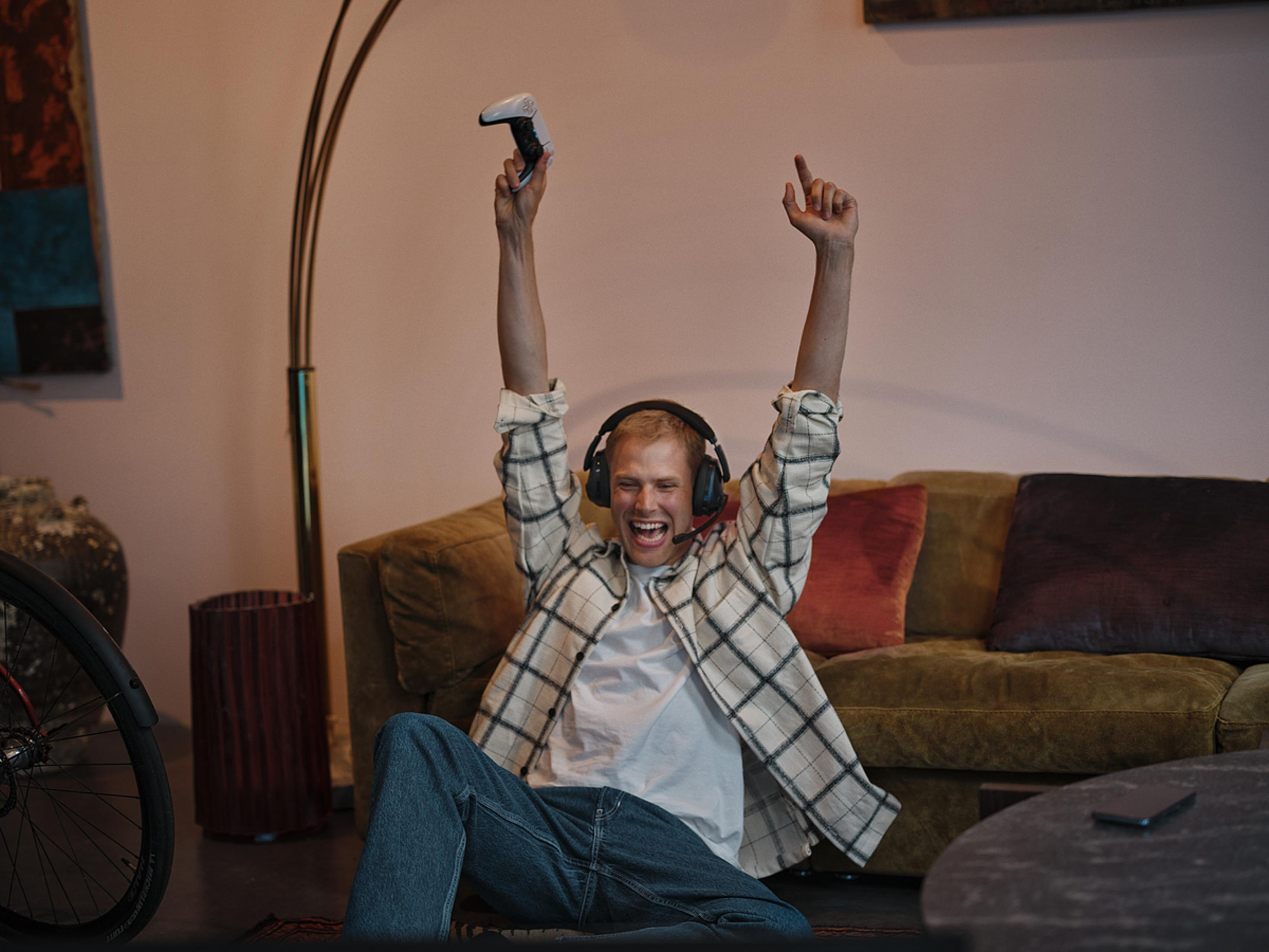 Ein Mann jubelt mit Controller und Kopfhörern auf dem Sofa.