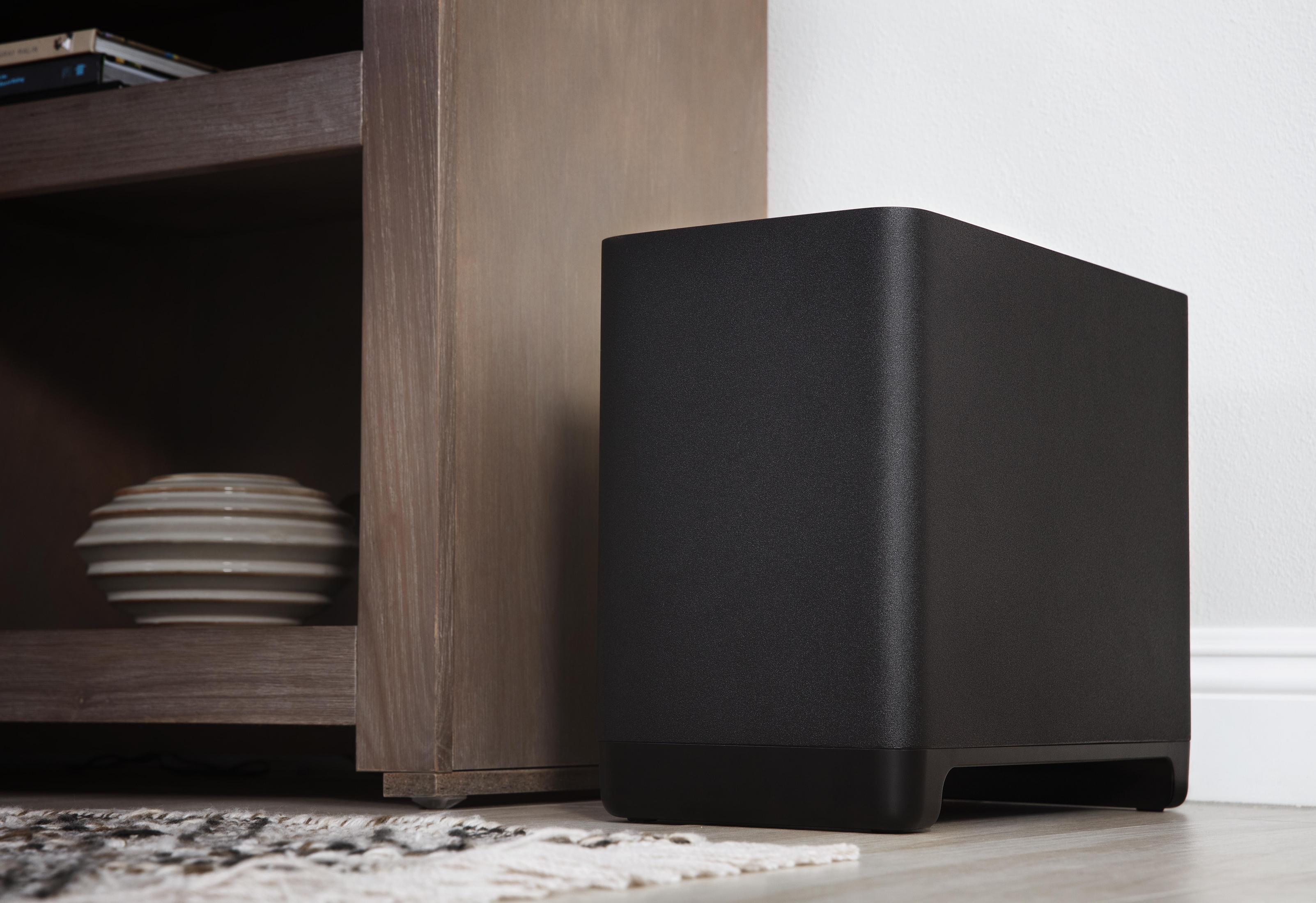 Schwarzer Subwoofer neben Holzschrank, auf einem Teppich.
