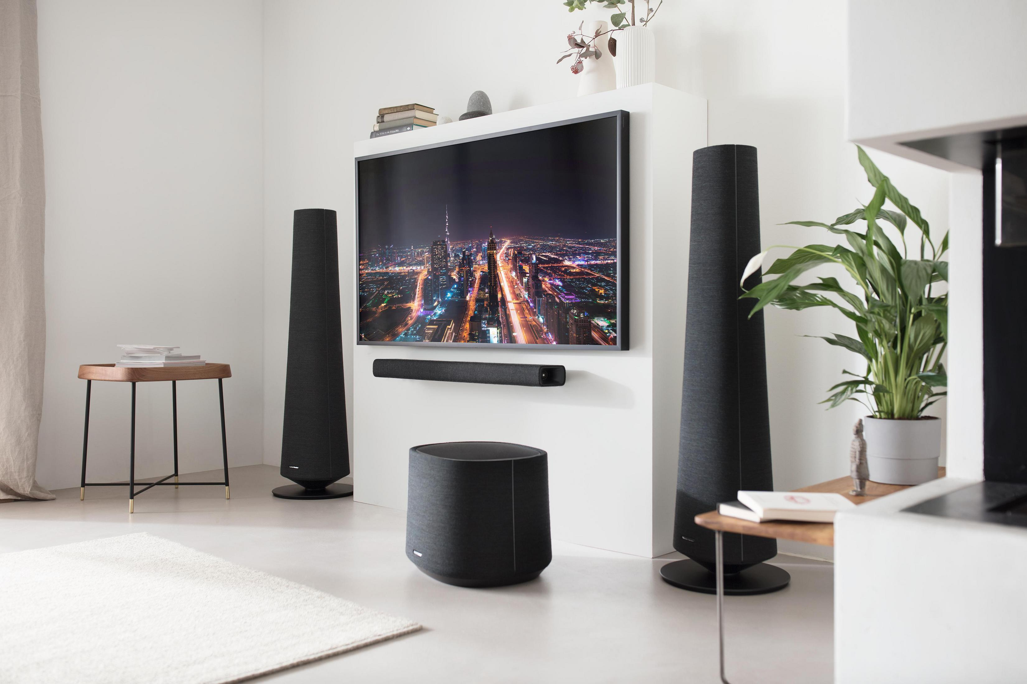 Wohnzimmer-Setup mit Lautsprechern, TV und Soundbar. Enthält einen Teppich und Pflanzen.