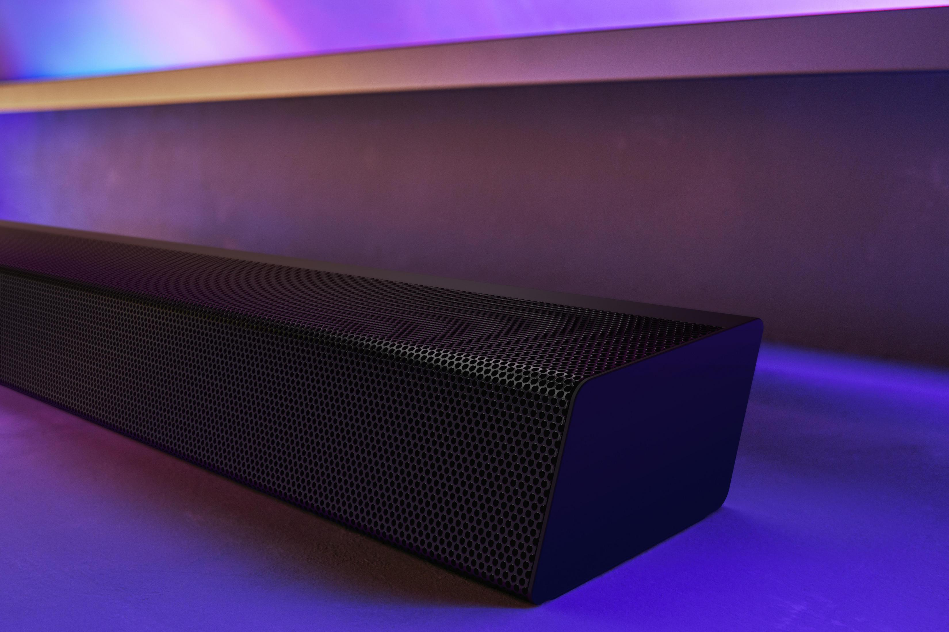 Una barra de sonido negra con un frente de malla. El fondo tiene iluminación púrpura y azul.
