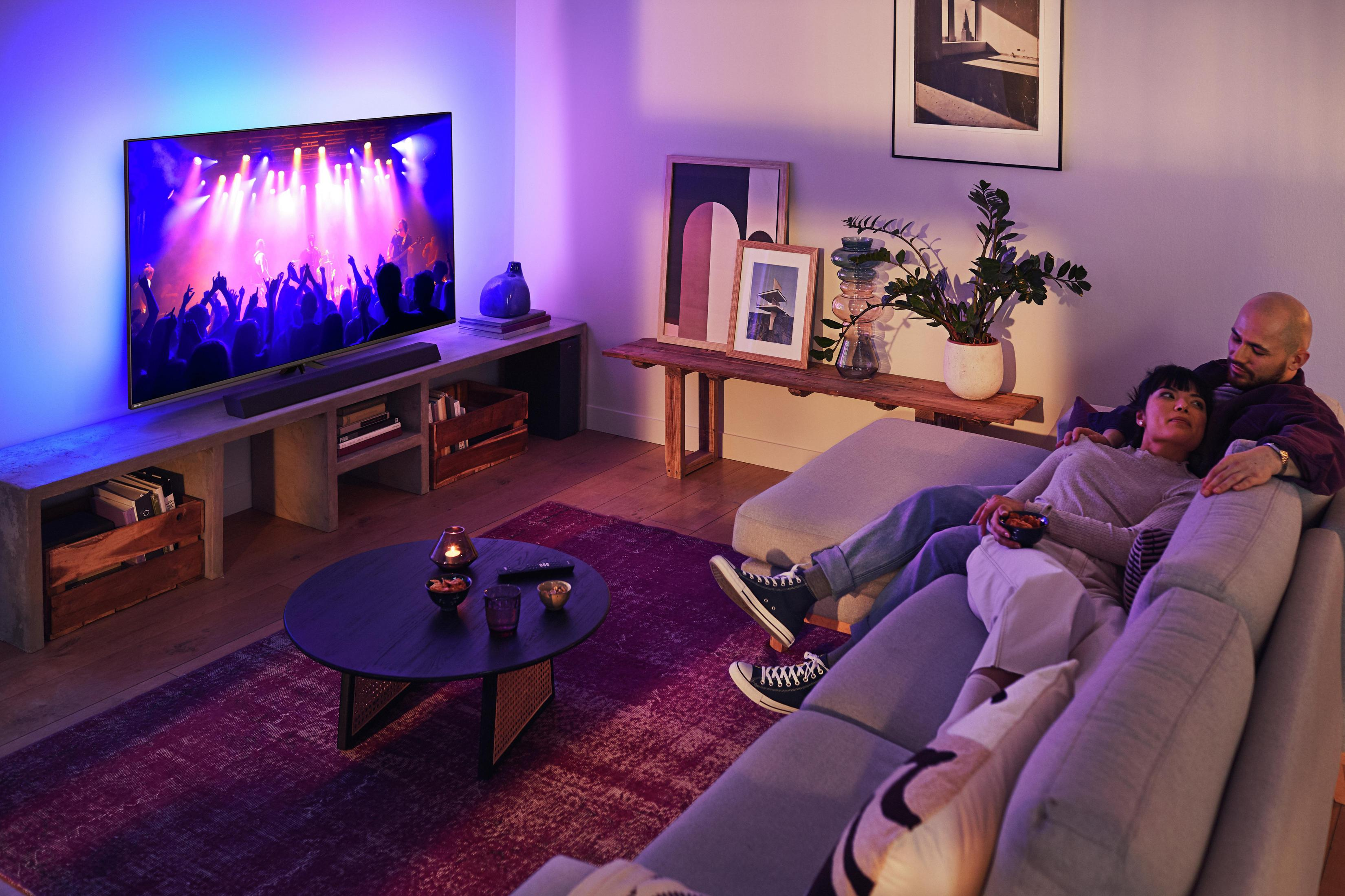 Una pareja ve la televisión encendida en una sala de estar, con elementos decorativos y lámparas.