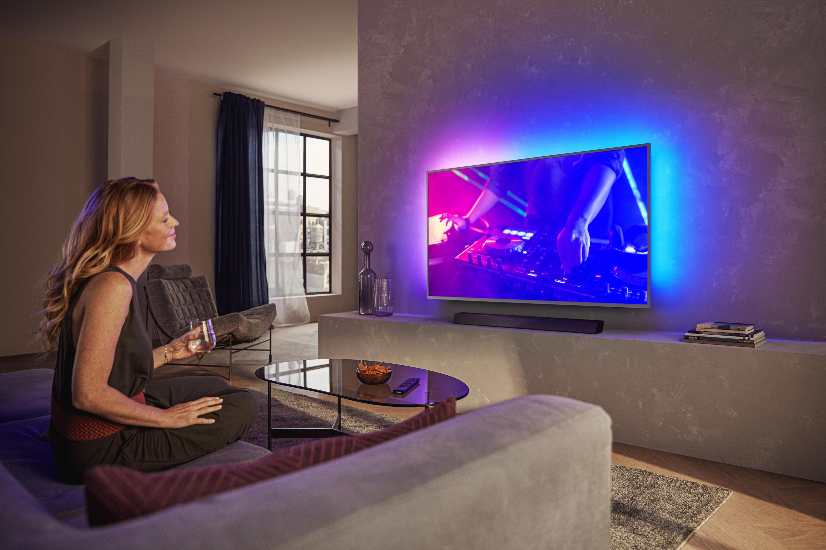 Mujer viendo la televisión con luces de colores. Aperitivos en la mesa. Salón.