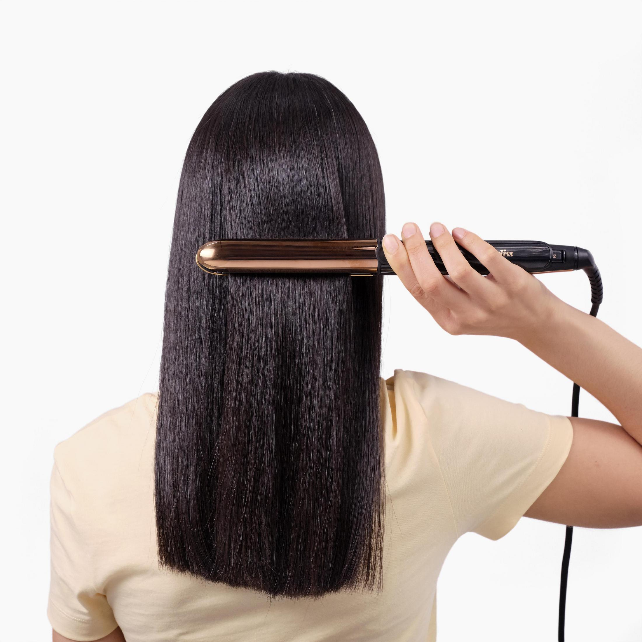 Una donna usa una piastra sui suoi lunghi capelli scuri, vista da dietro.