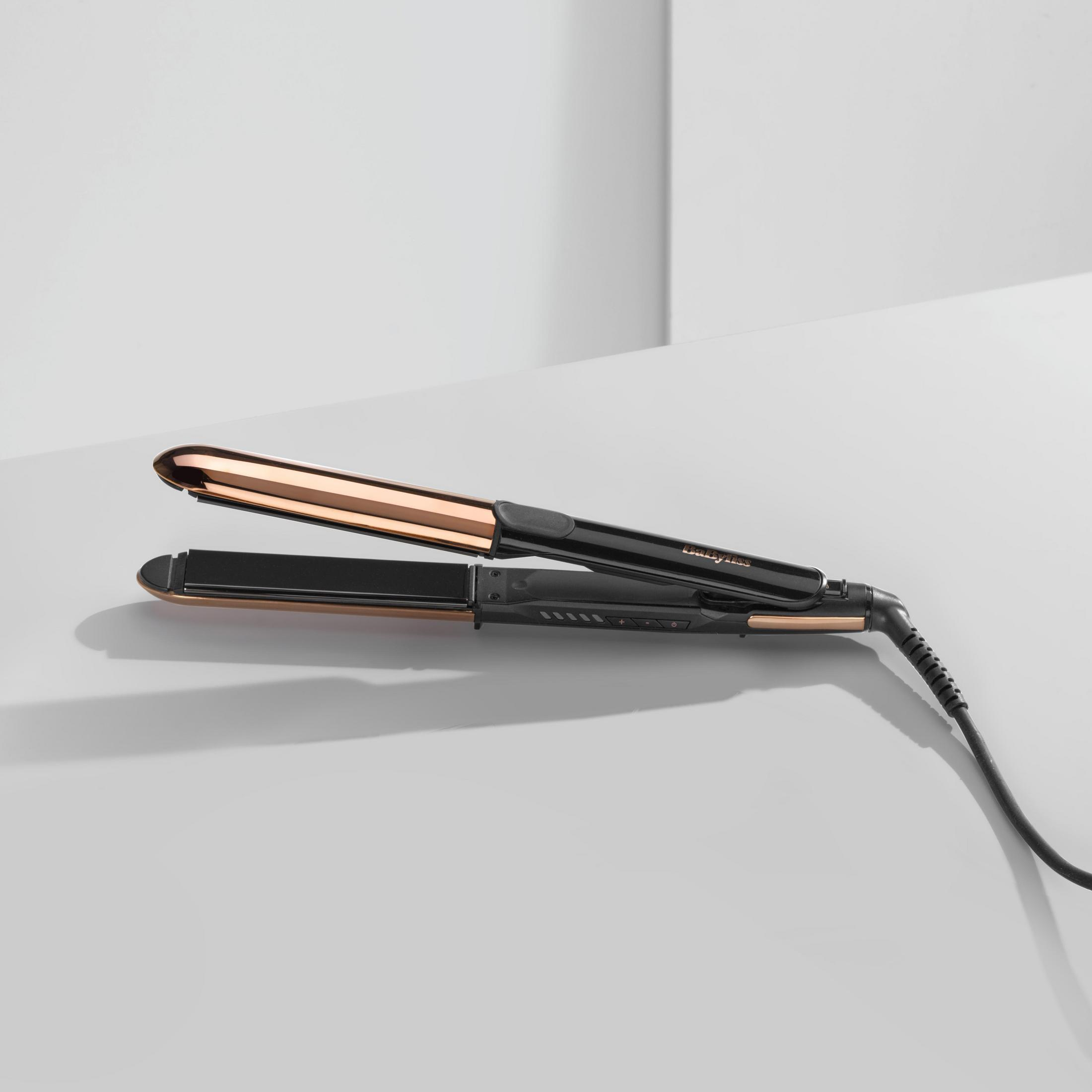 Piastra per capelli nera con piastra riscaldante oro rosa su una superficie bianca.