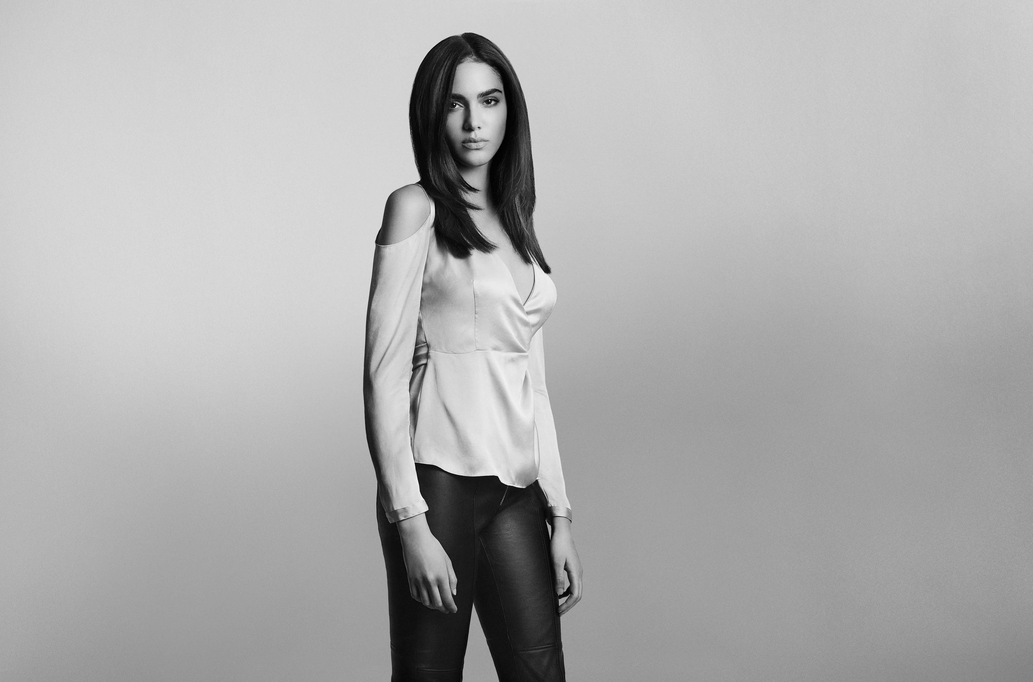 Czarno-białe zdjęcie kobiety w jasnej bluzce i czarnych spodniach, pozującej.