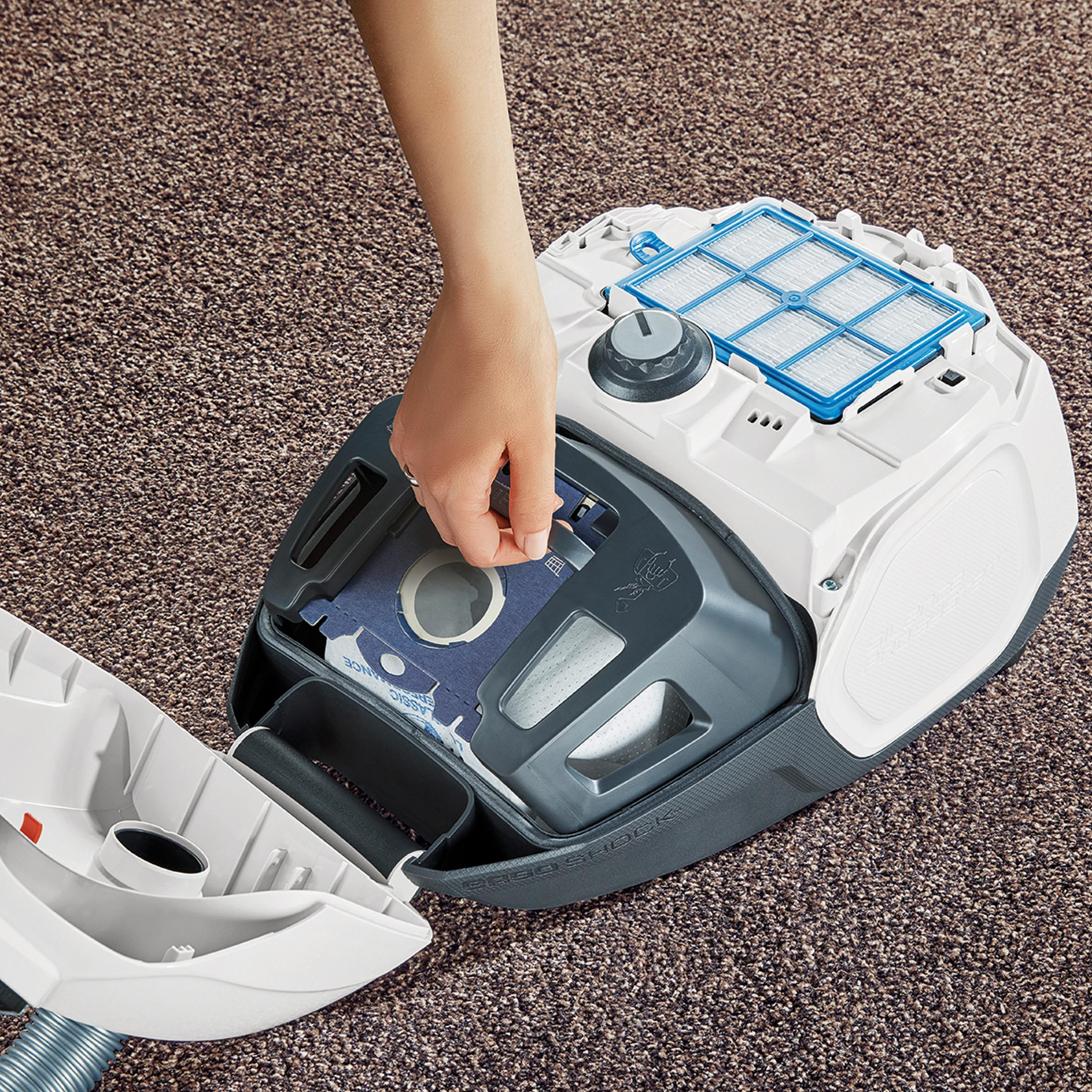 Ręka wkładająca worek do odkurzacza z tekstem i szczegółami.